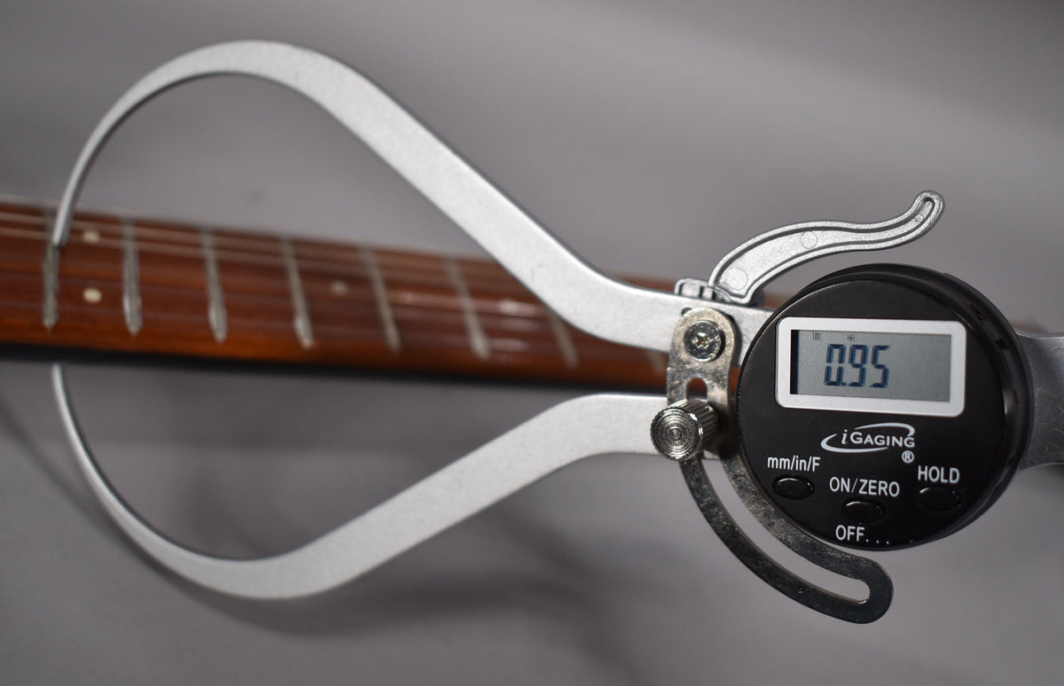 A digital caliper measures the guitar's fretboard, displaying "0.95" on its screen.