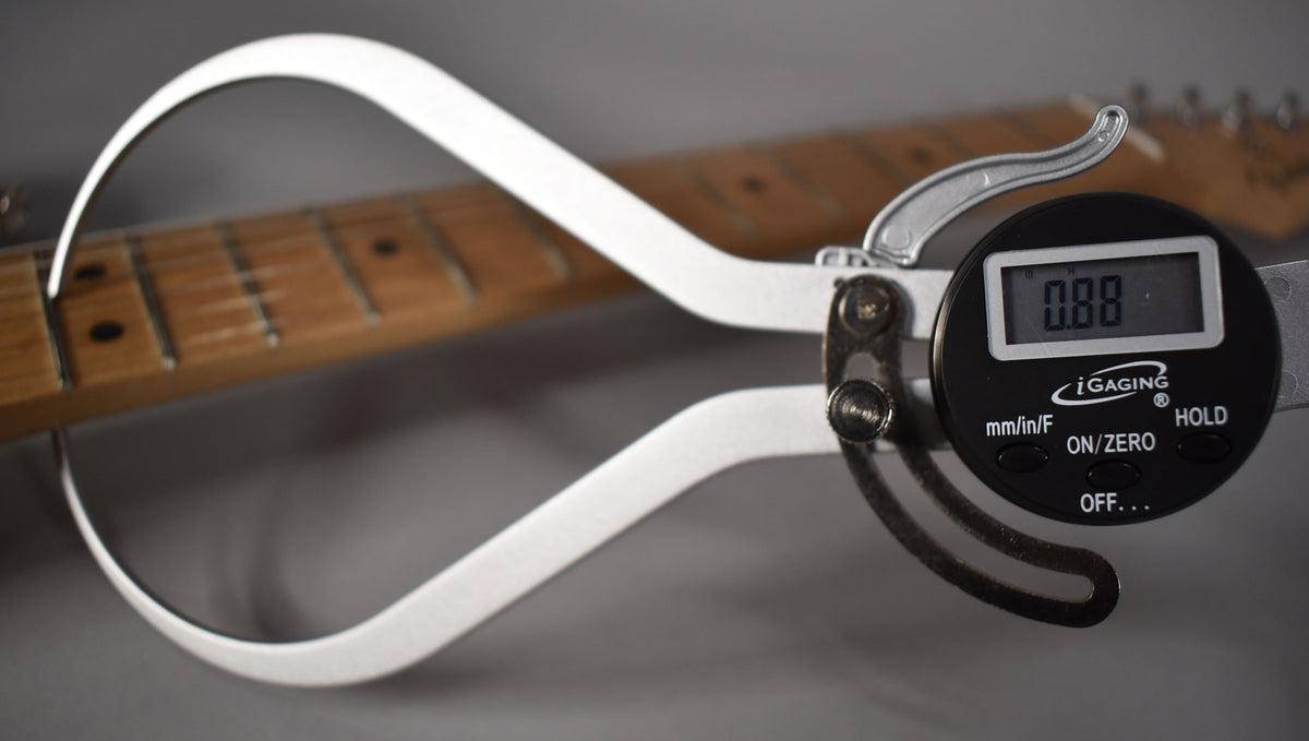 A digital caliper measures the Olympic White Stratocaster's fretboard, showing a reading of 0.88.