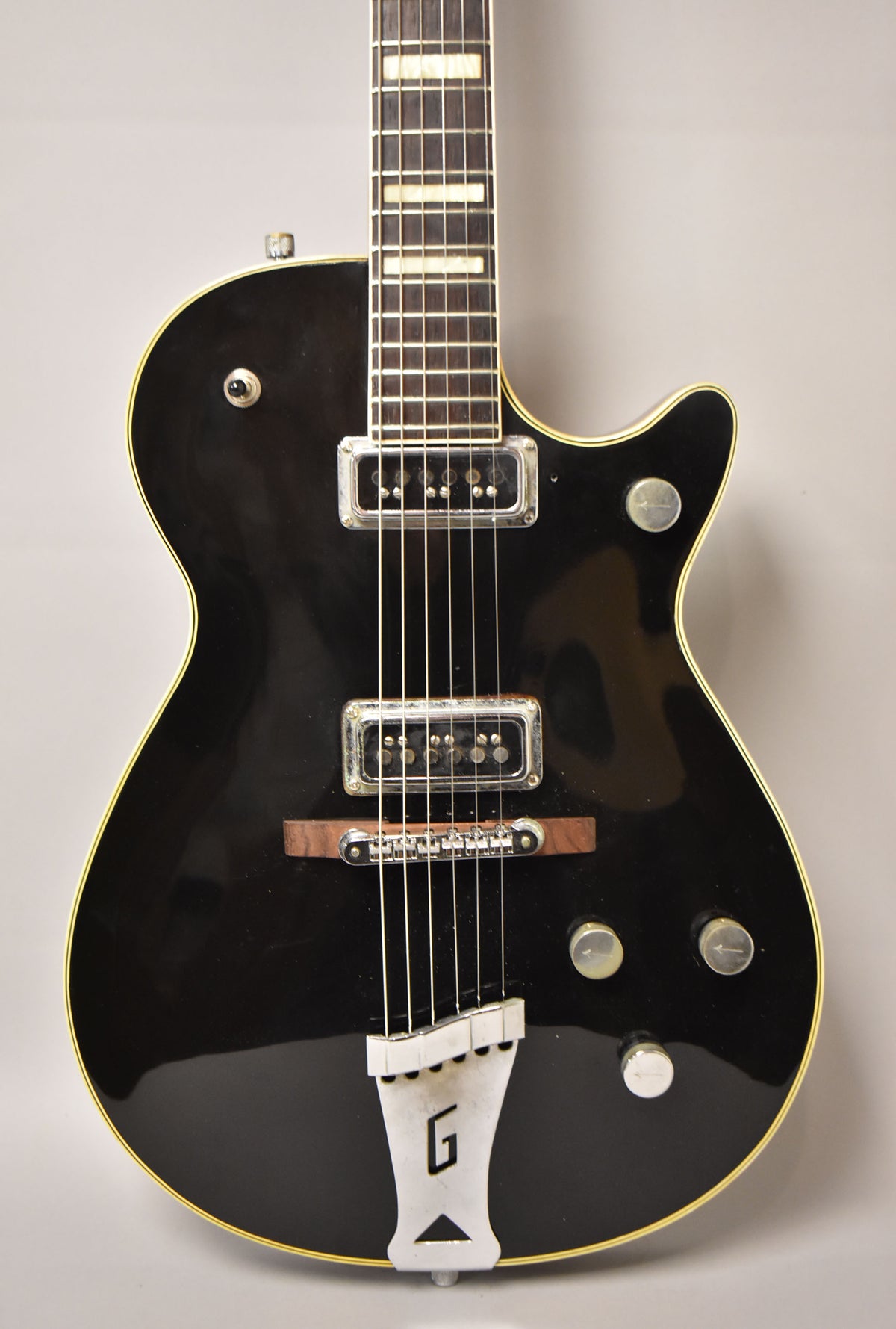 Black electric guitar, full body shot, with two chrome pickups, a wooden bridge, and a chrome "G" tailpiece.