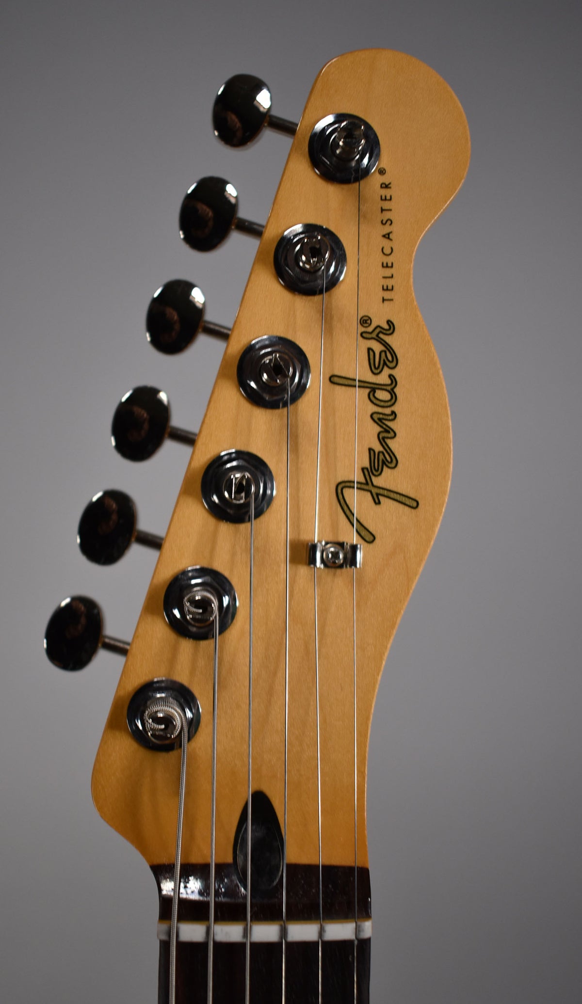 Close-up of the Telecaster's light wood headstock, angled left, showing six chrome tuners, a string tree, and dark fretboard.