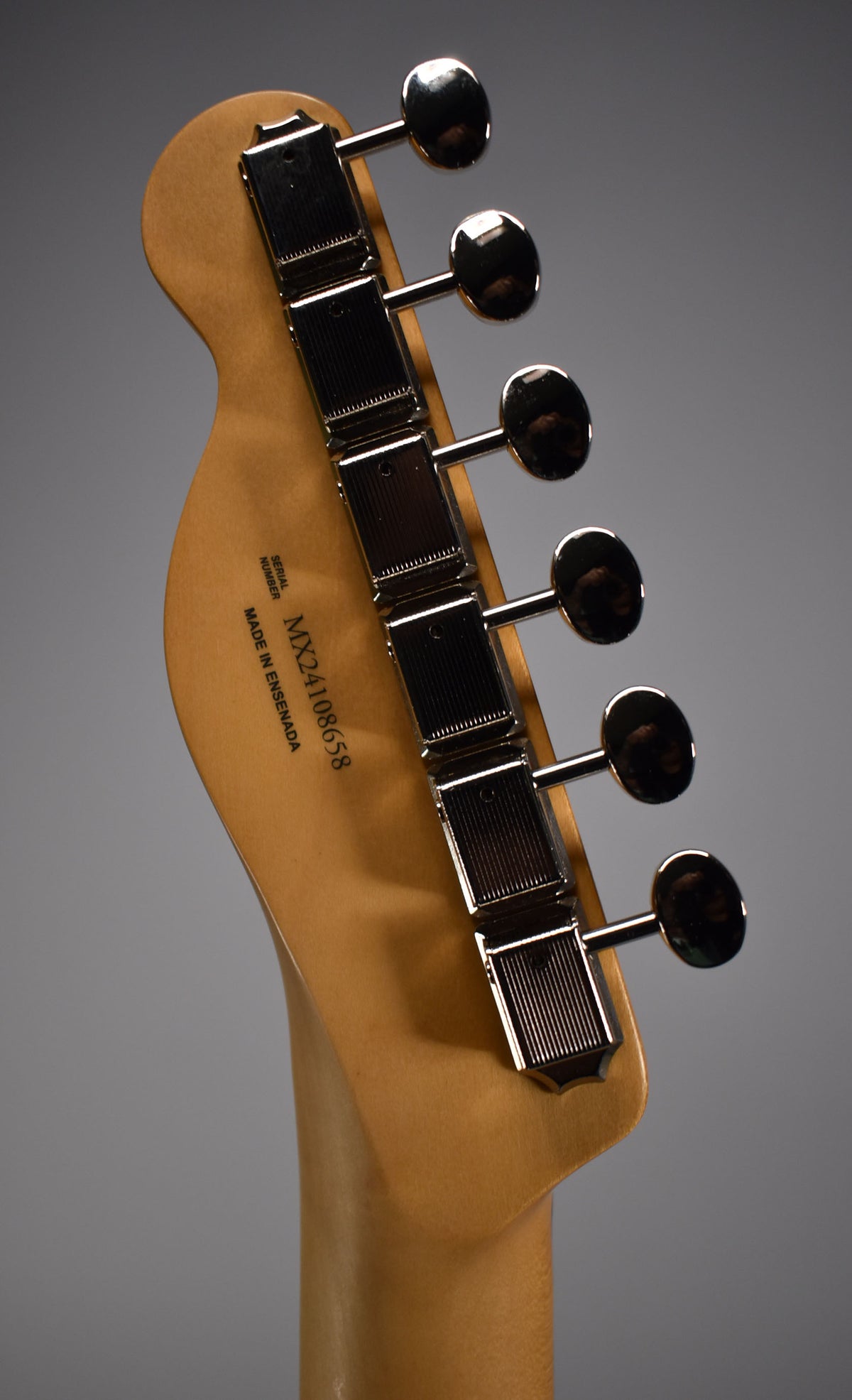 The back of a light brown guitar headstock with six chrome tuning machines, angled from the top right.