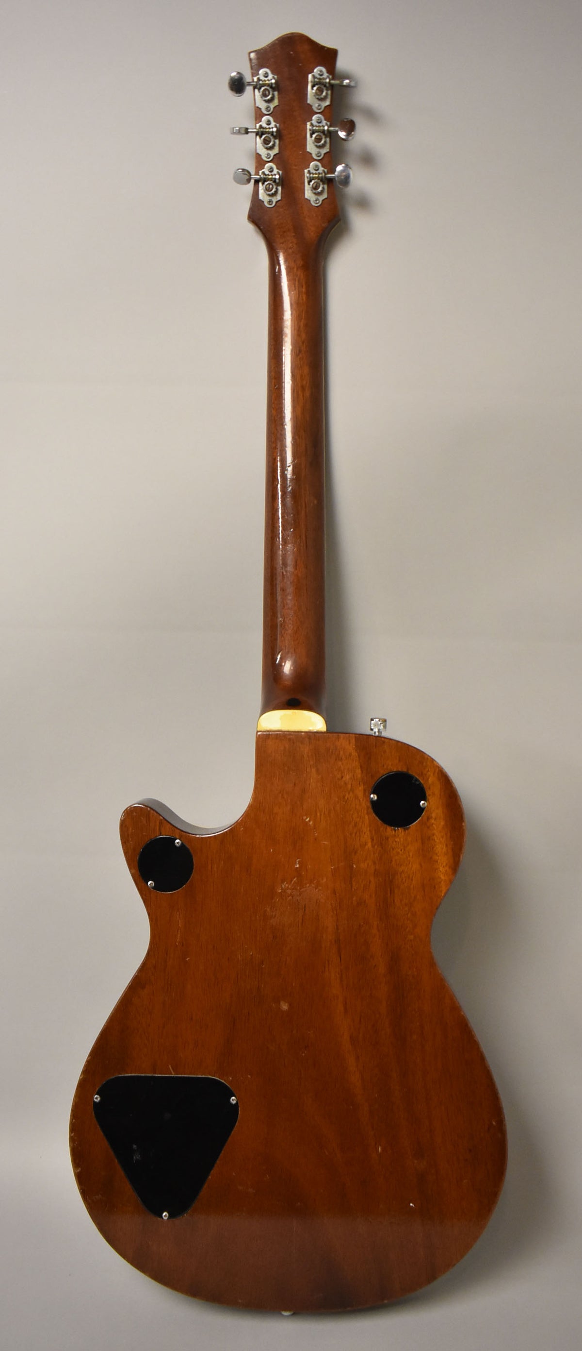 The guitar's back is dark brown with a glossy finish, showing wear and scratches, with three black control plates.