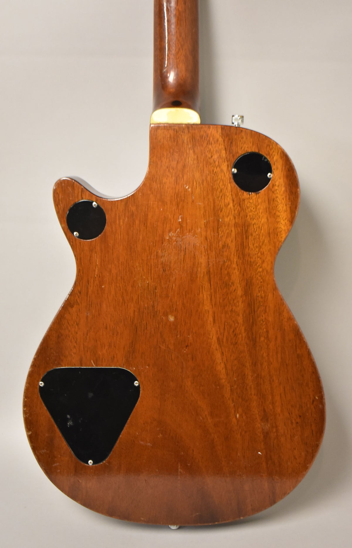 The guitar's mahogany back shows visible wear, scratches, and three black control plates, with a light brown neck joint.