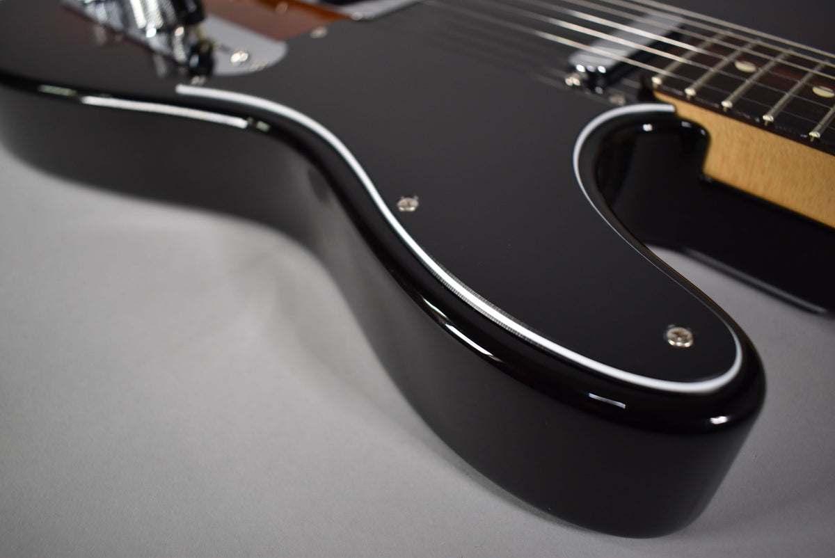 A close-up of a black guitar body with white binding, showing part of the pickguard, strings, and a light-colored neck.
