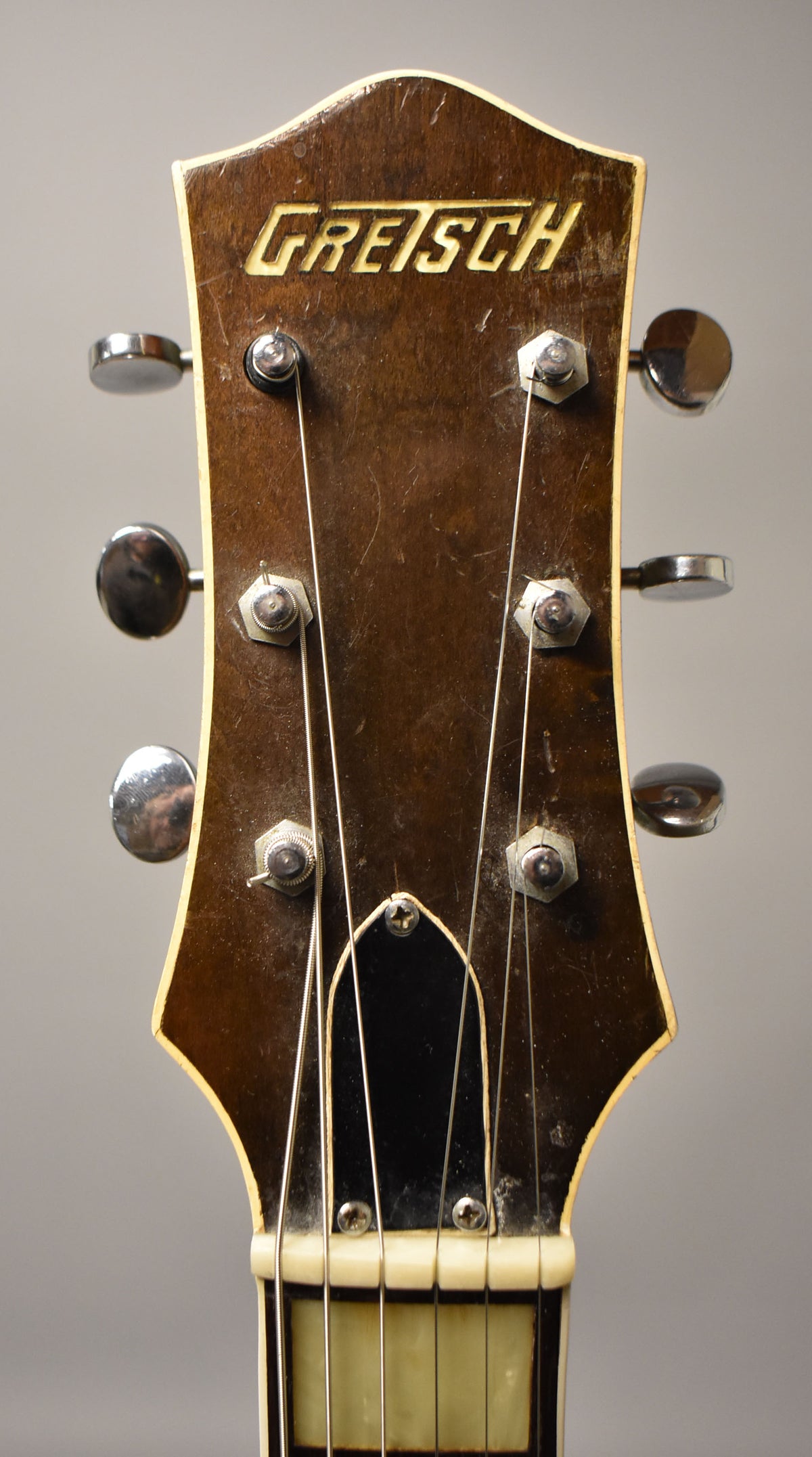 Close-up of the guitar's dark brown headstock, showing six chrome tuners, a black truss rod cover, and heavy finish wear.