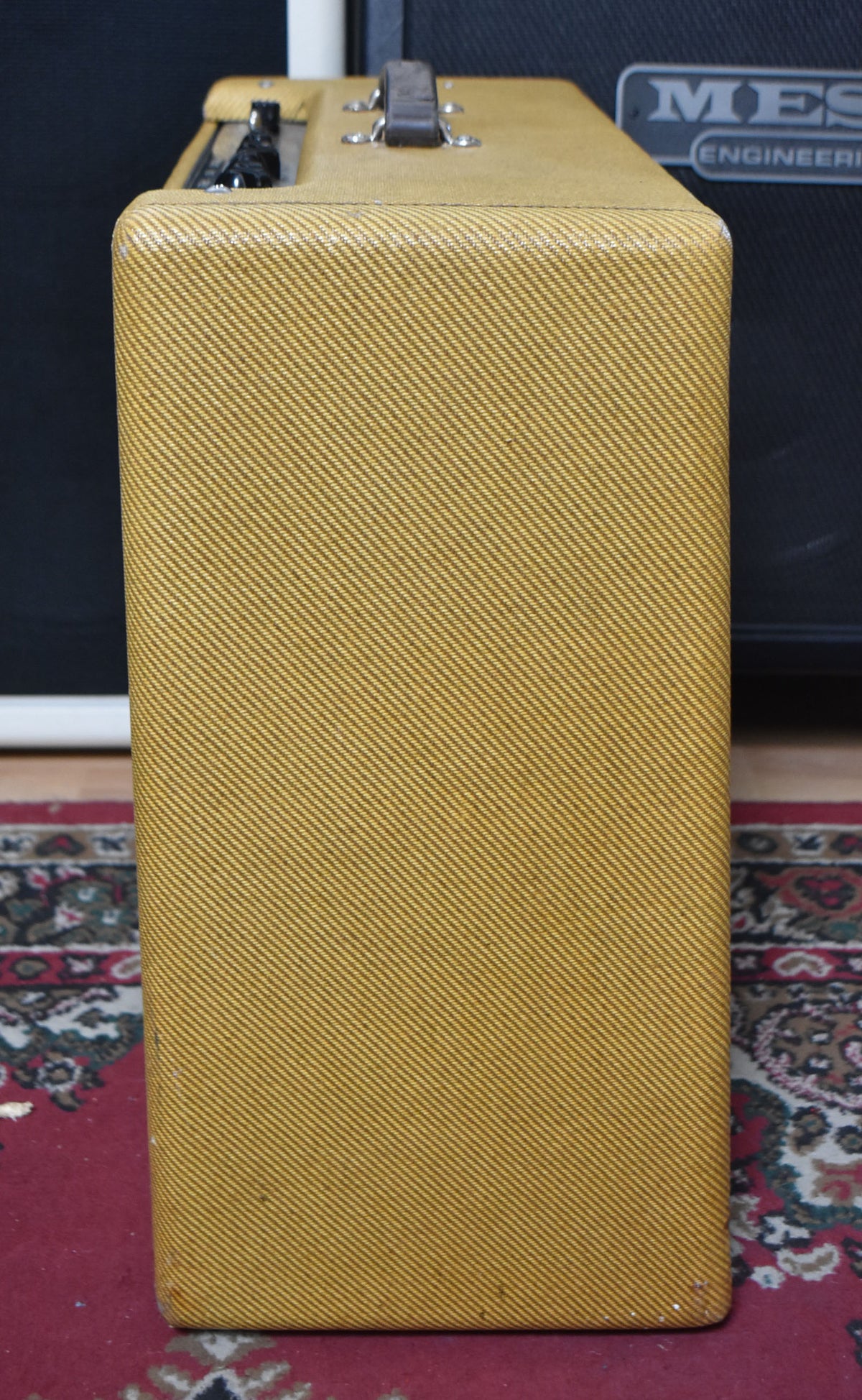 The tweed amplifier is shown from the right side, revealing a brown leather handle and minor scuffs on the top and bottom edges.