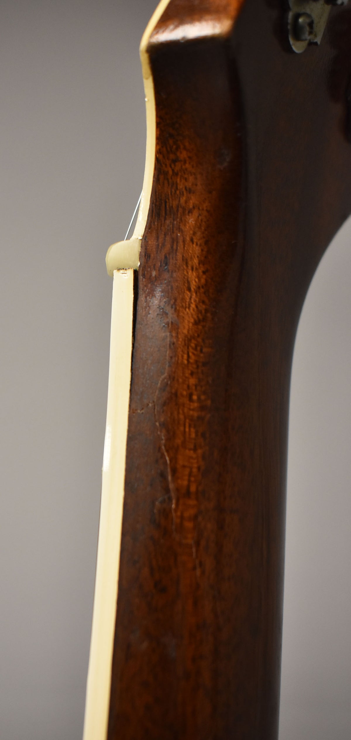 Close-up of the guitar's dark brown neck and headstock joint, showing finish wear and checking, with a cream binding and nut.