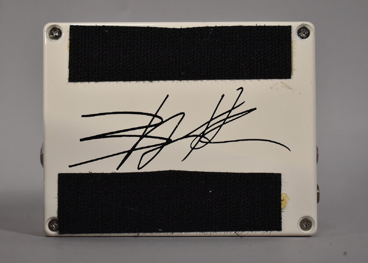 The white pedal's underside is shown, featuring two black velcro strips, a large black signature, and visible wear near the bottom right.
