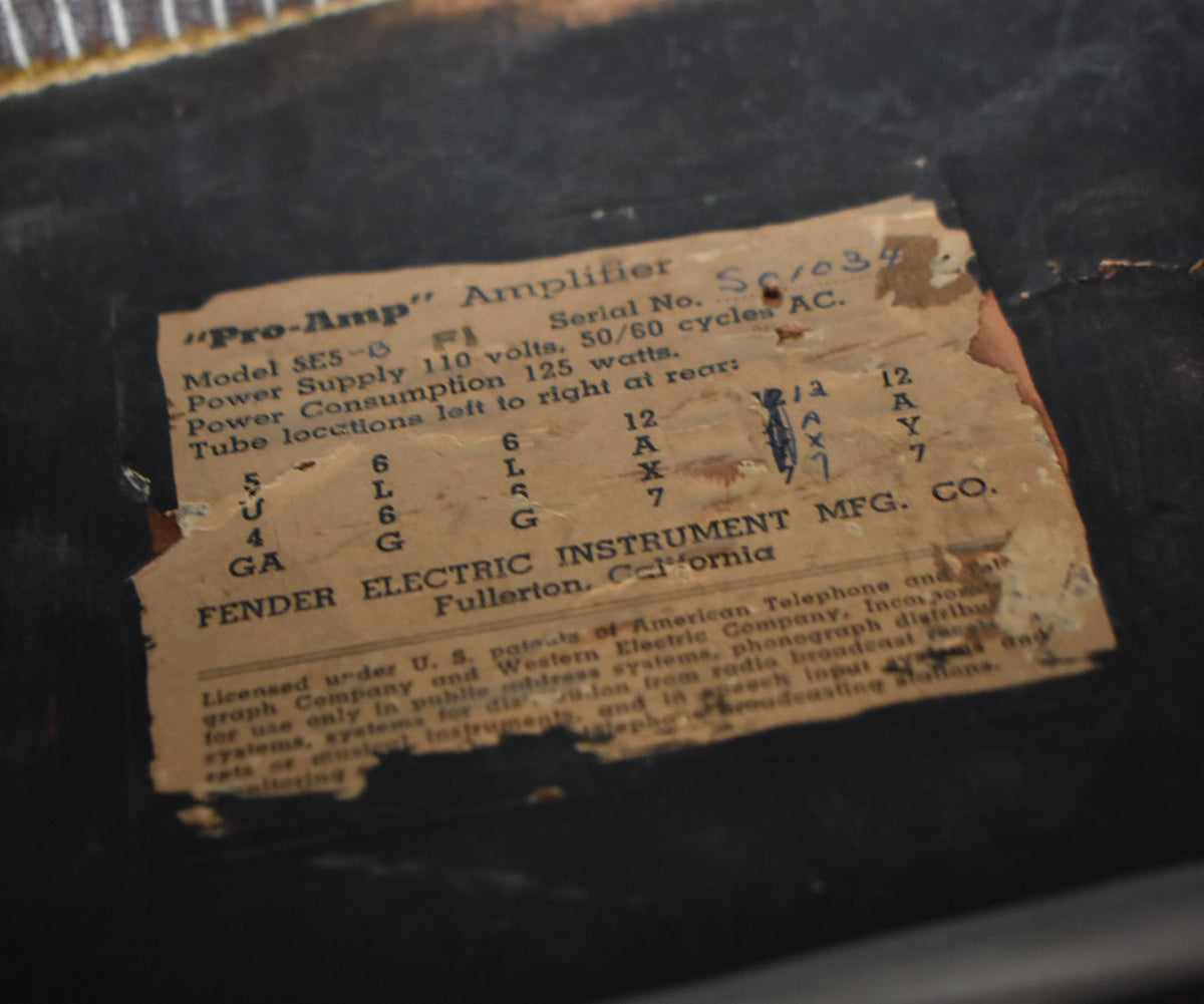 Close-up of the amp's worn, yellowed paper label, showing text and numbers, with torn edges against a dark background.