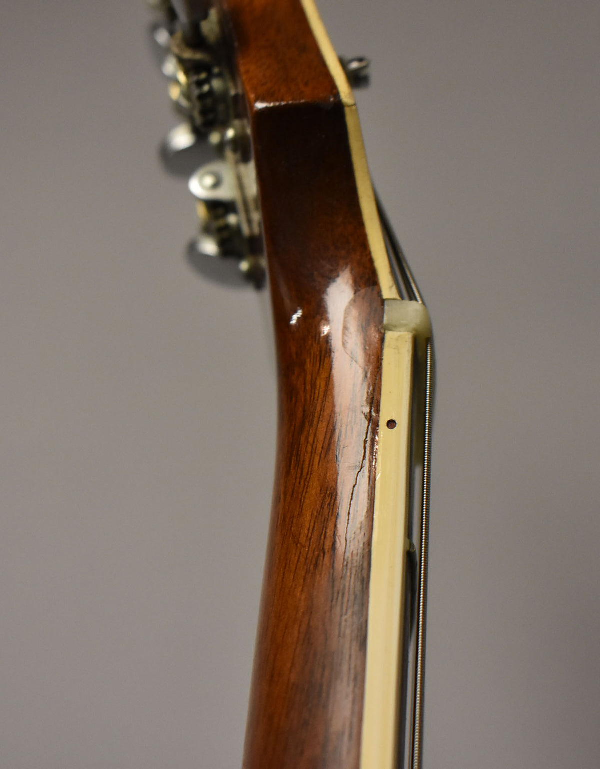Close-up of the guitar's neck from the side, showing a glossy brown finish, cream binding, and a visible crack near the nut.