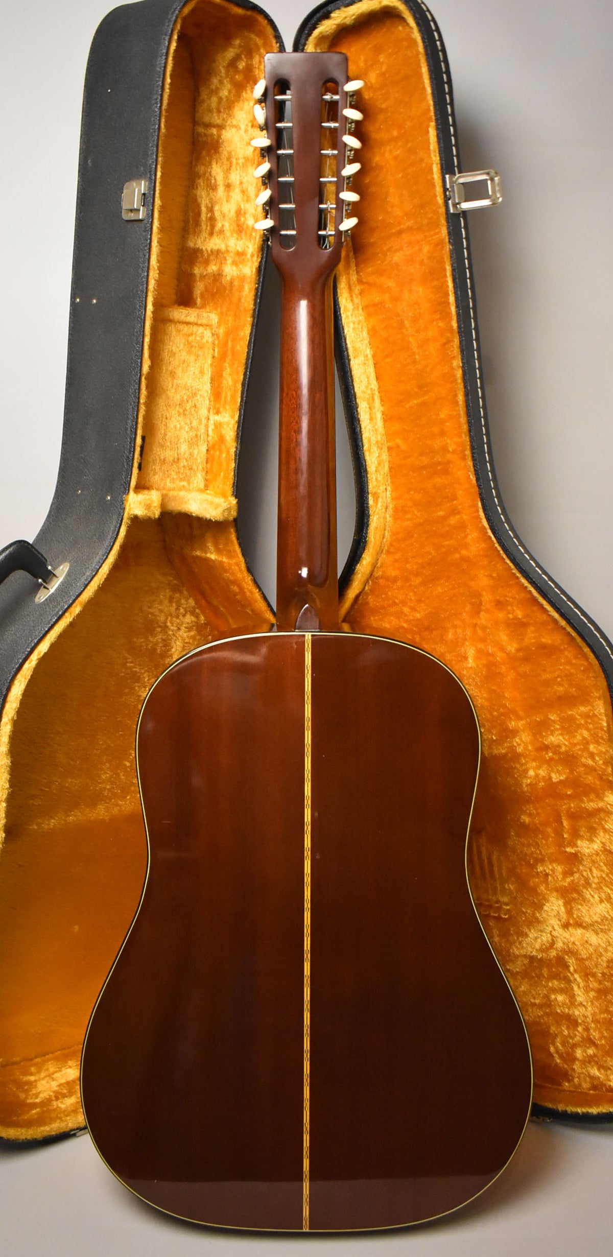 Rear view of the dark brown acoustic guitar, showing the headstock with 12 white tuning pegs, neck, and body with a light center stripe.