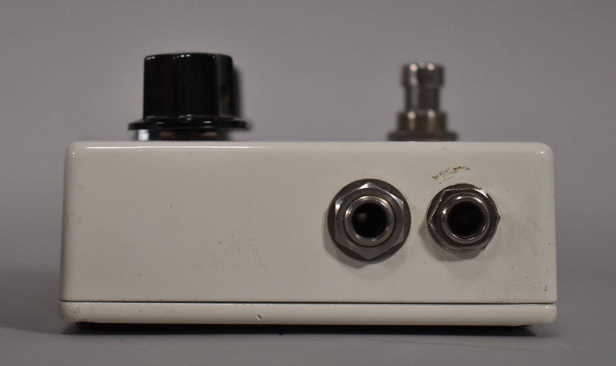 The white pedal's right side is shown, featuring two input jacks, a black control knob, and a footswitch, with some scuffs.