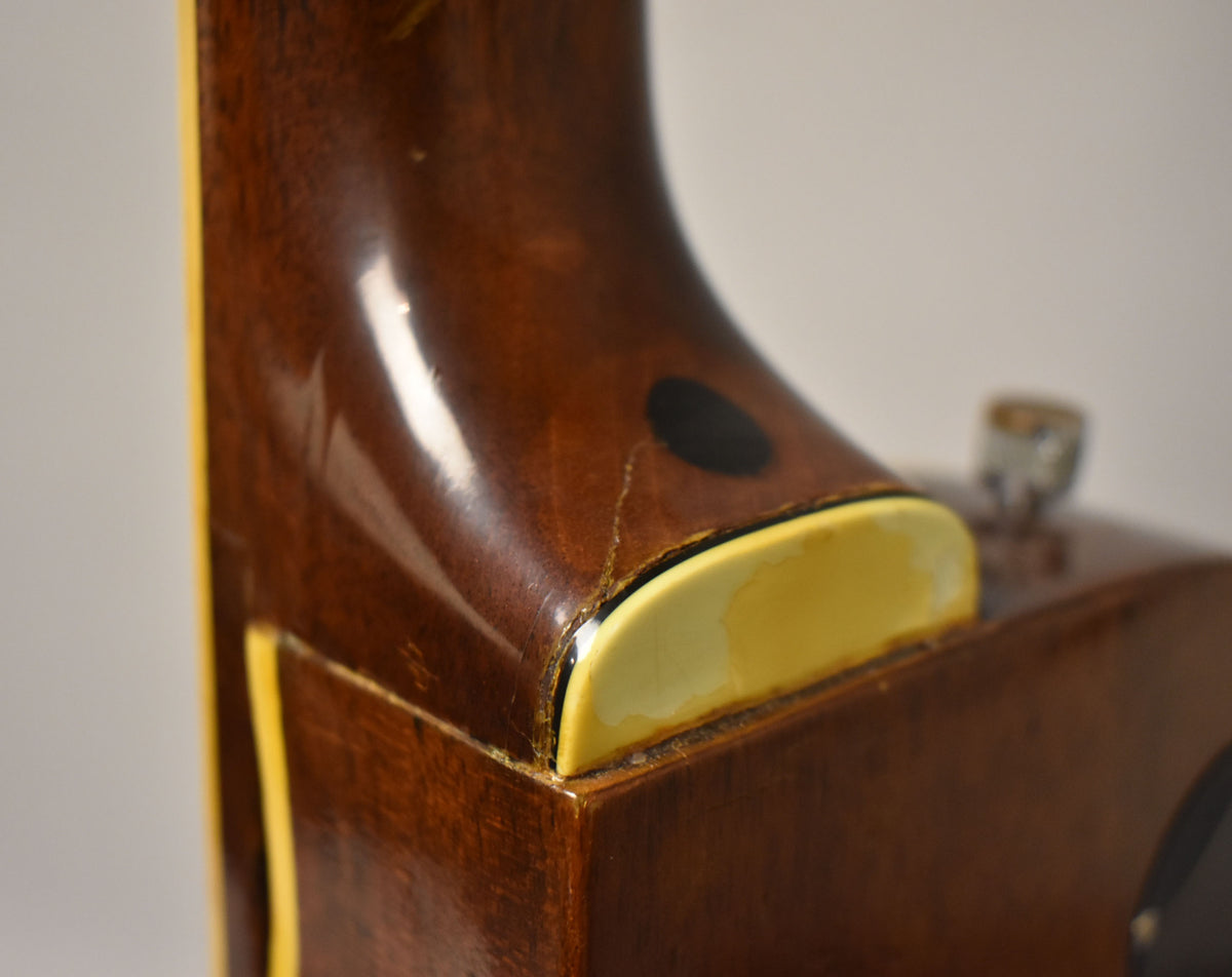 Close-up of the guitar's neck heel, showing a dark brown finish, cream binding, and visible finish checking and wear.