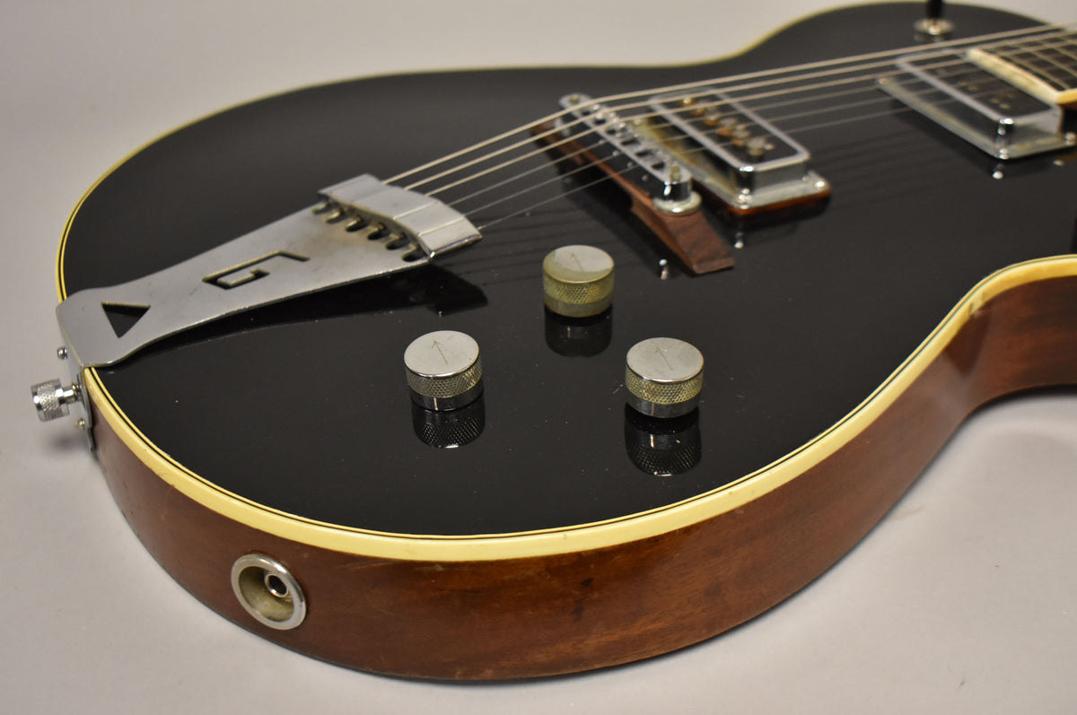 Close-up of the guitar's lower bout, showing the black glossy finish, chrome tailpiece, three knurled control knobs, and output jack.