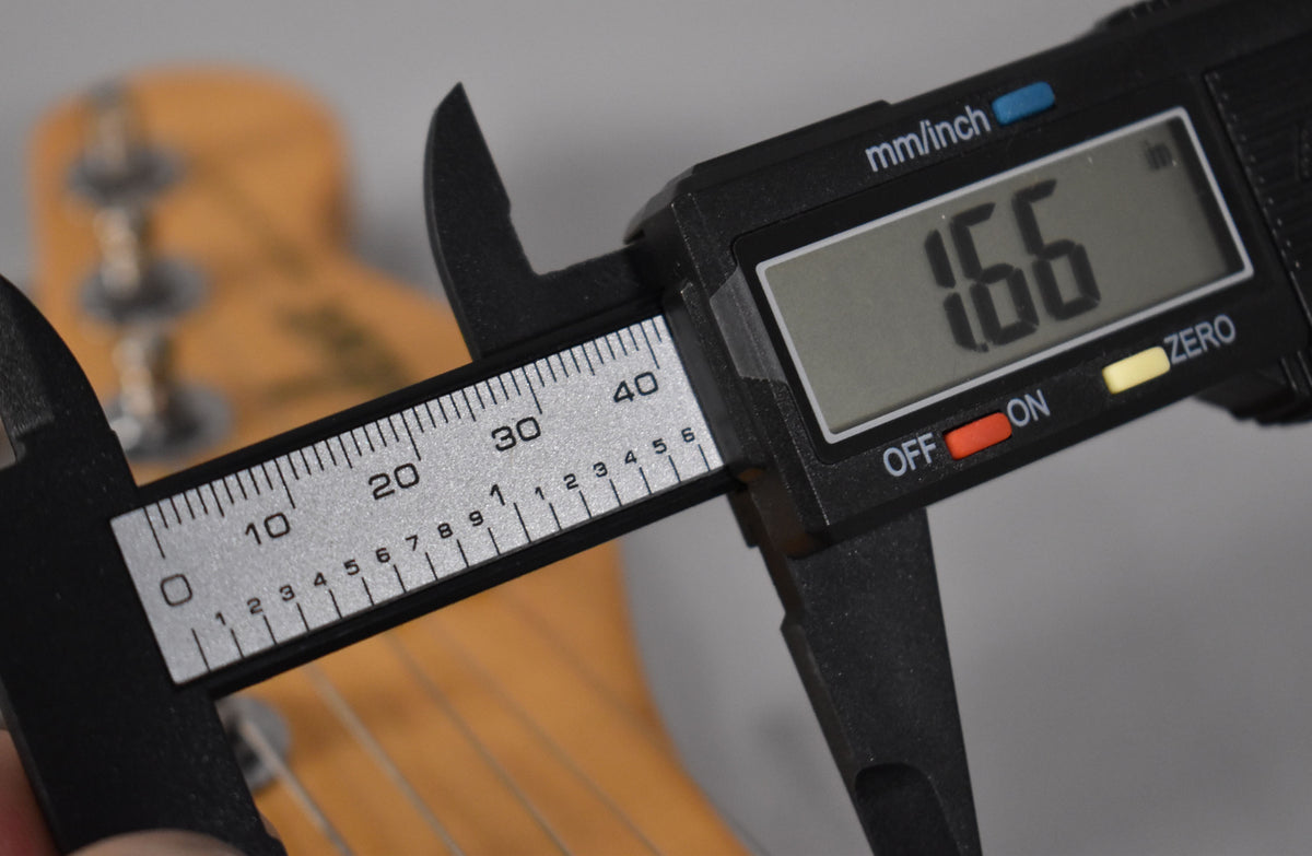 A digital caliper measures the Telecaster's nut width at 1.66 inches, with the headstock and tuning pegs blurred in the background.