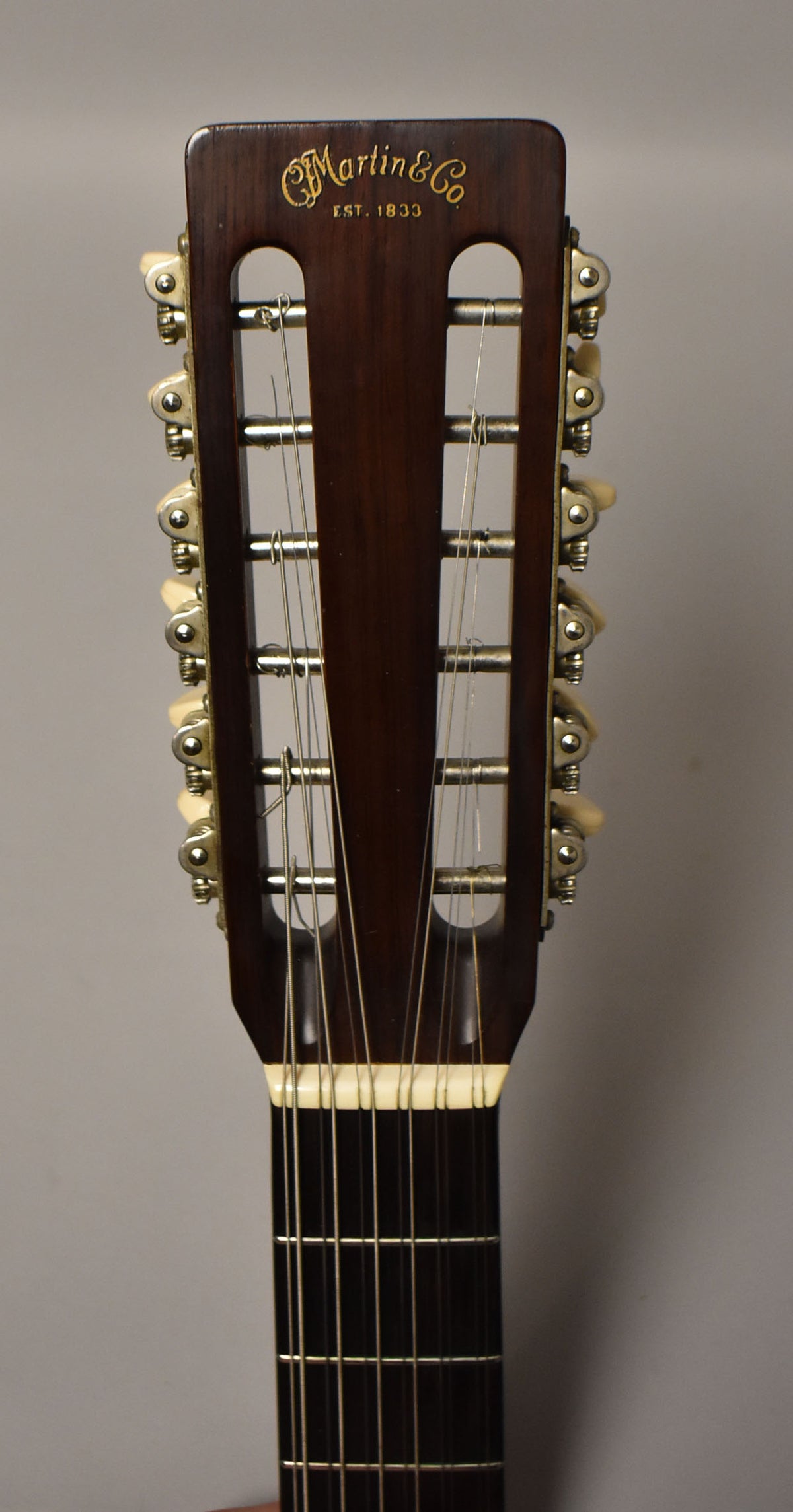 Close-up of the dark brown slotted headstock and upper fretboard, showing 12 strings, 12 ivory-colored tuning pegs, and light wear.