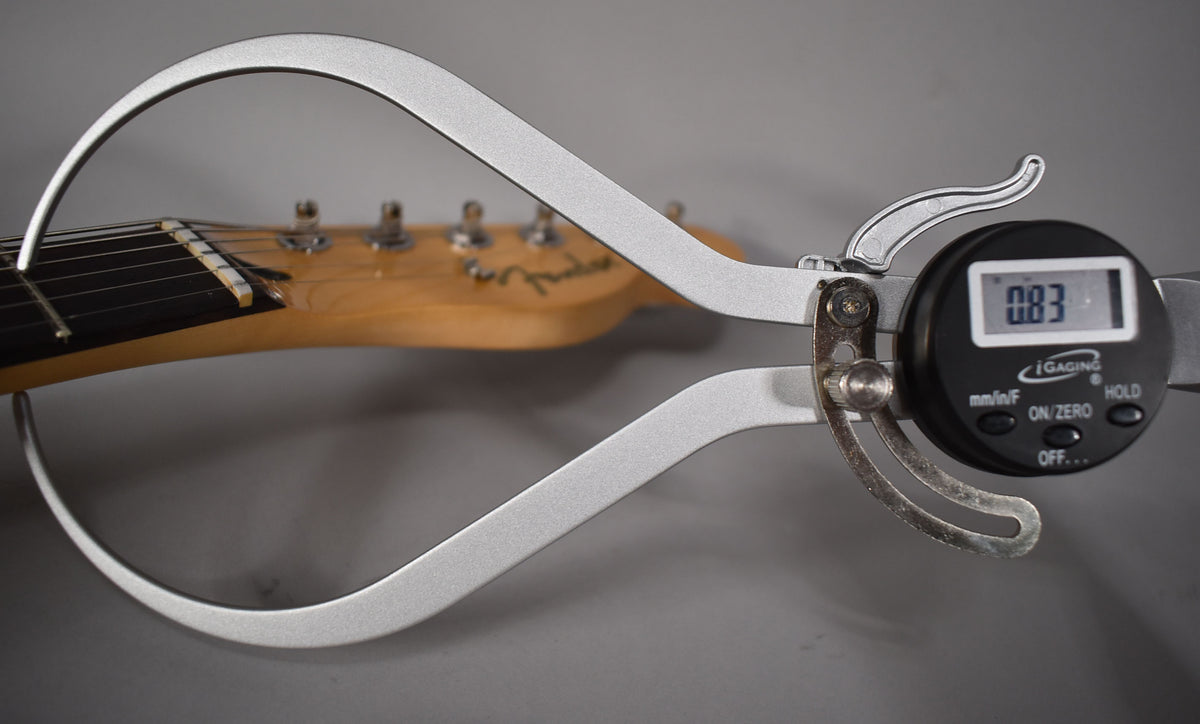 A digital caliper measures the nut width of the Telecaster's maple neck and dark fretboard, showing 0.83 on its display.