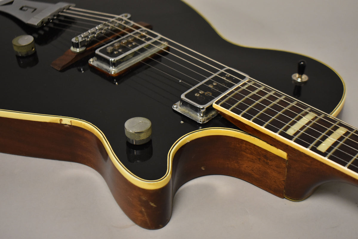 Close-up of the black guitar body and neck, showing chrome pickups, two knurled knobs, a toggle switch, and binding wear.