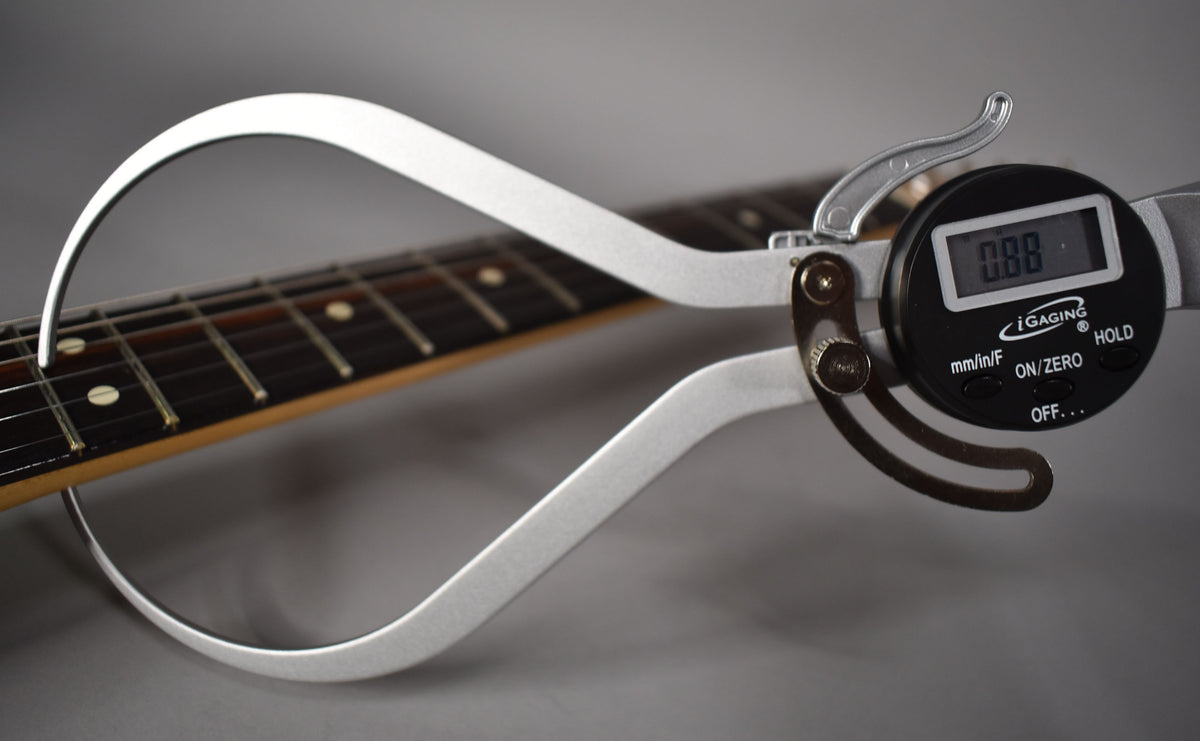 Digital calipers measure the fret height of a Telecaster's dark rosewood fretboard with cream dot inlays.