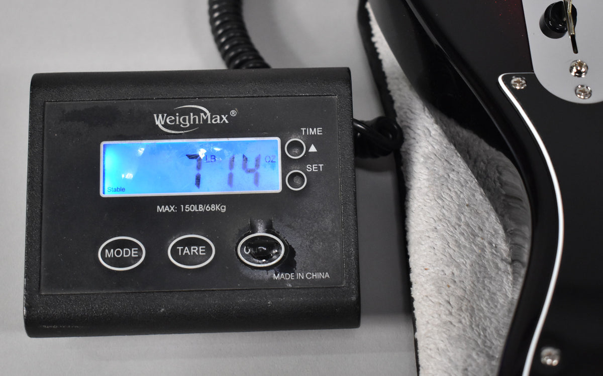 A black digital scale displays "7 LB 14 OZ" next to the lower bout of a black and red sparkle sunburst Telecaster.