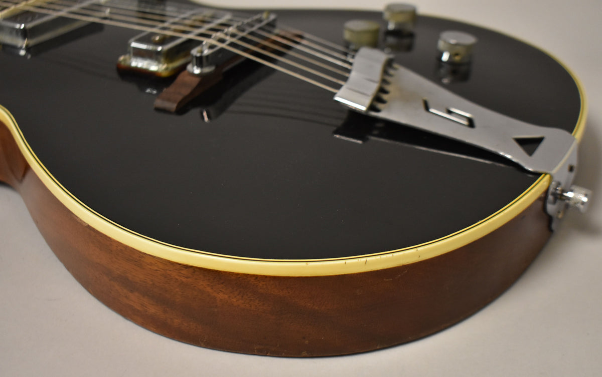 Close-up of the black guitar body's lower bout, showing the cream binding, mahogany sides, chrome tailpiece, and two control knobs.