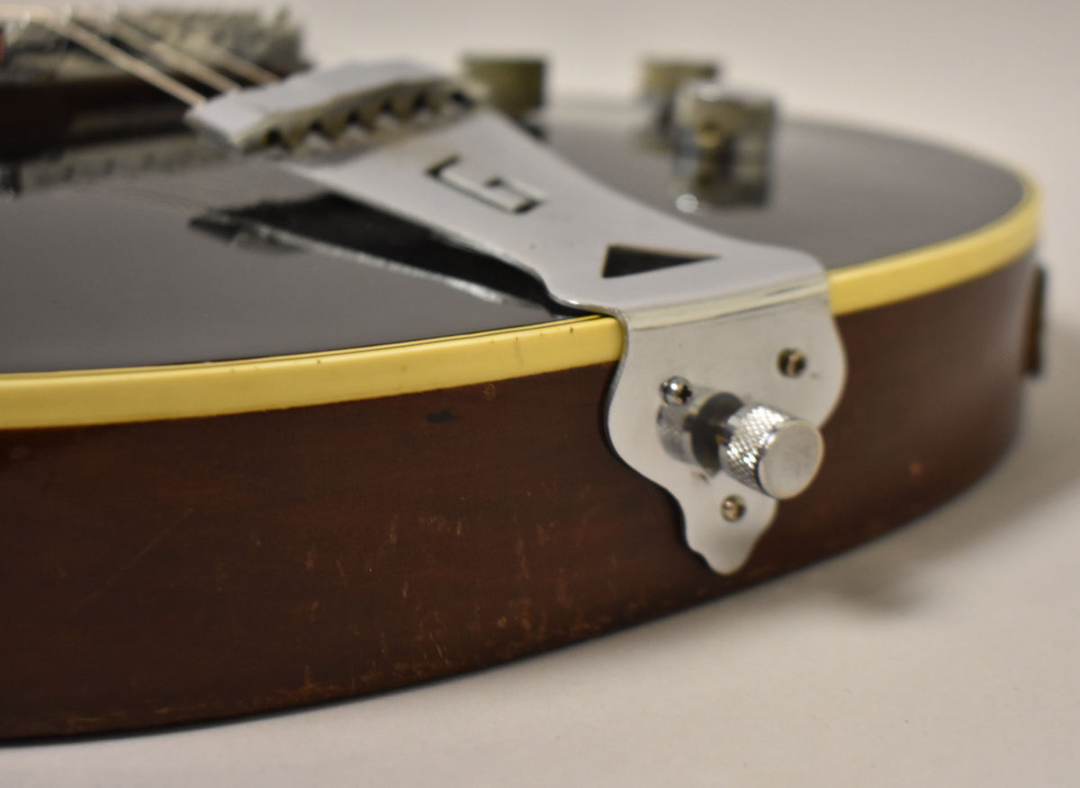 Close-up of the guitar's lower bout, showing the black top, cream binding, dark brown sides with wear, and chrome tailpiece.
