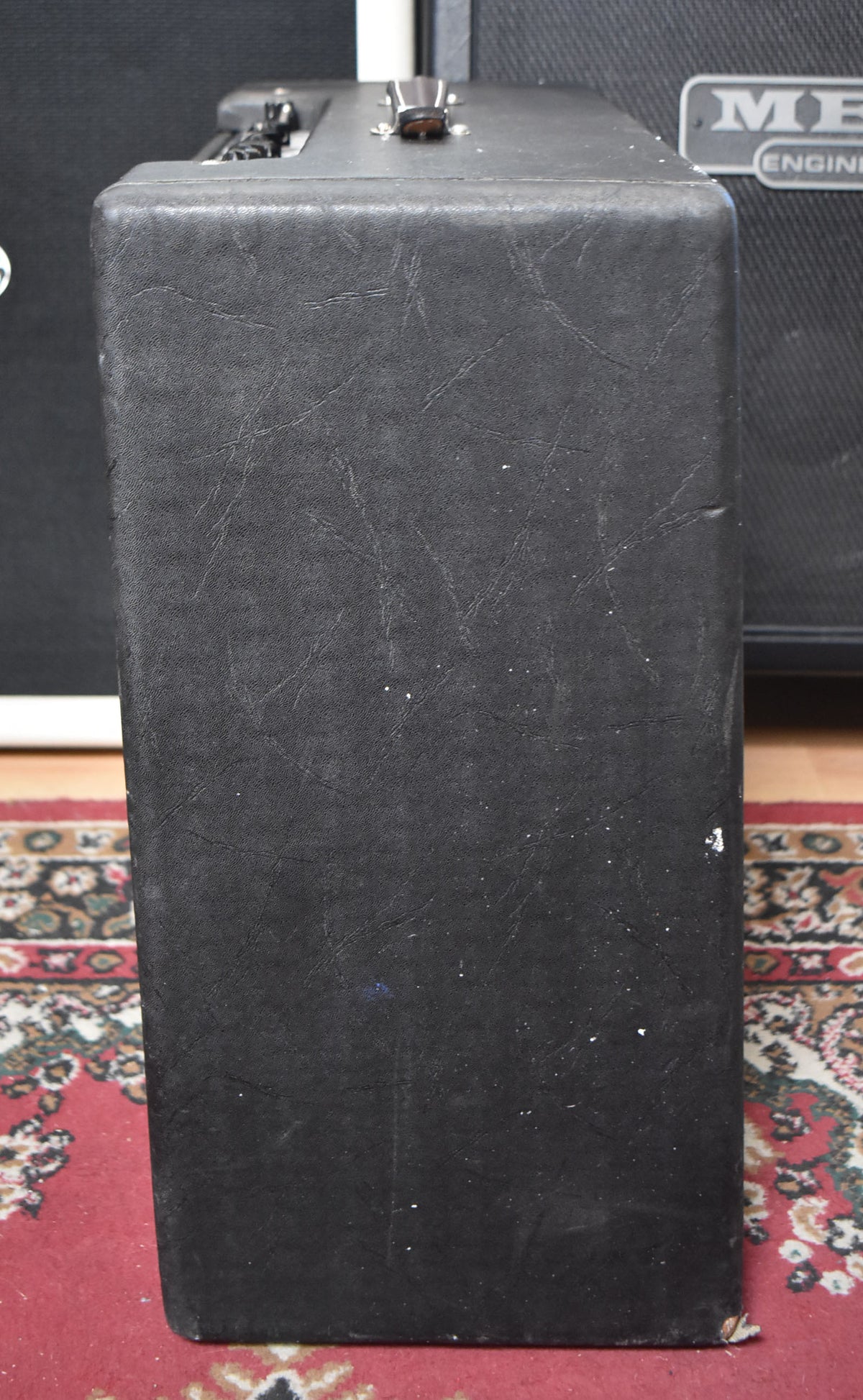 The black amp is viewed from the side, showing its textured tolex covering with visible scuffs, white marks, and a few small tears.