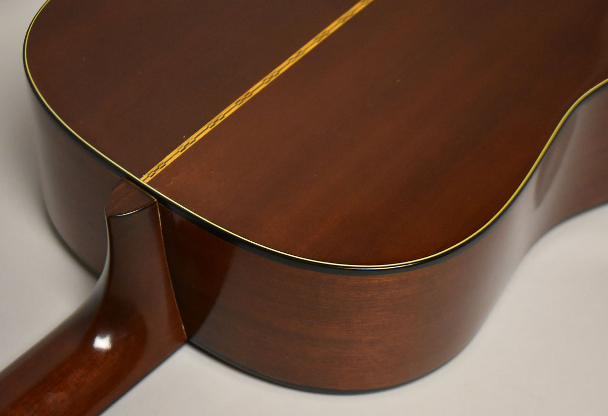 The guitar's dark brown back and side are visible, with a light wood center strip and yellow binding around the edges.