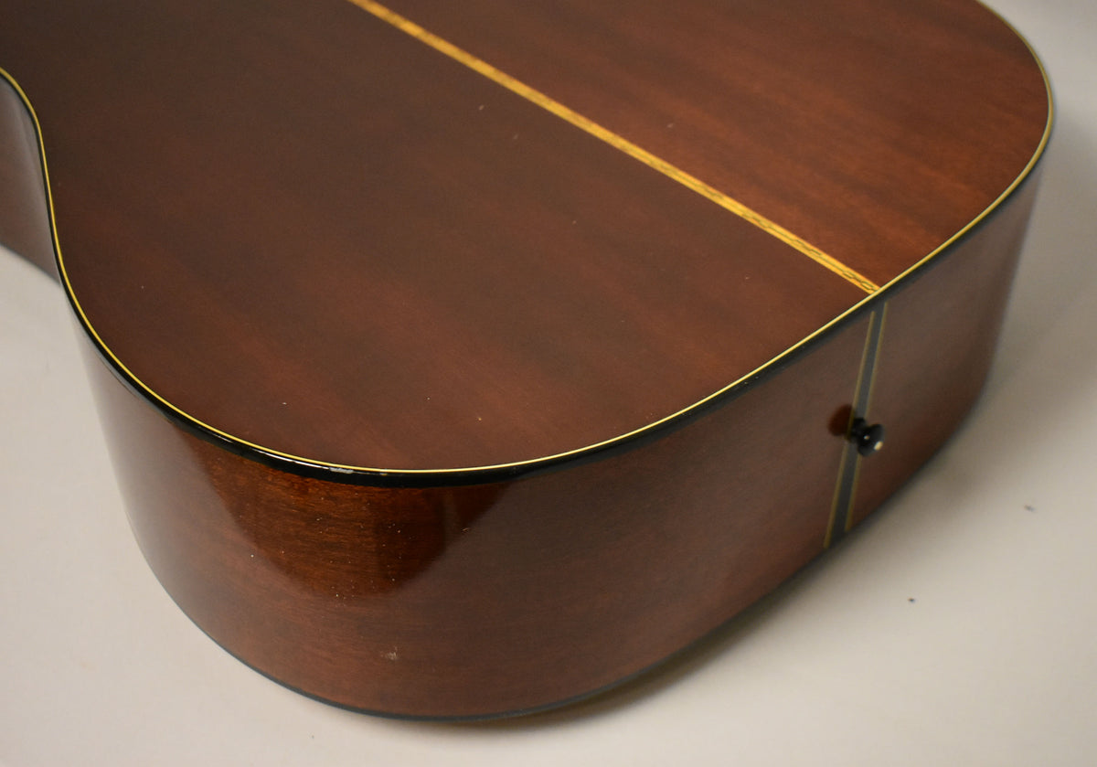 The lower bout of a natural finish acoustic guitar, showing the dark brown back and side, with a black end pin.