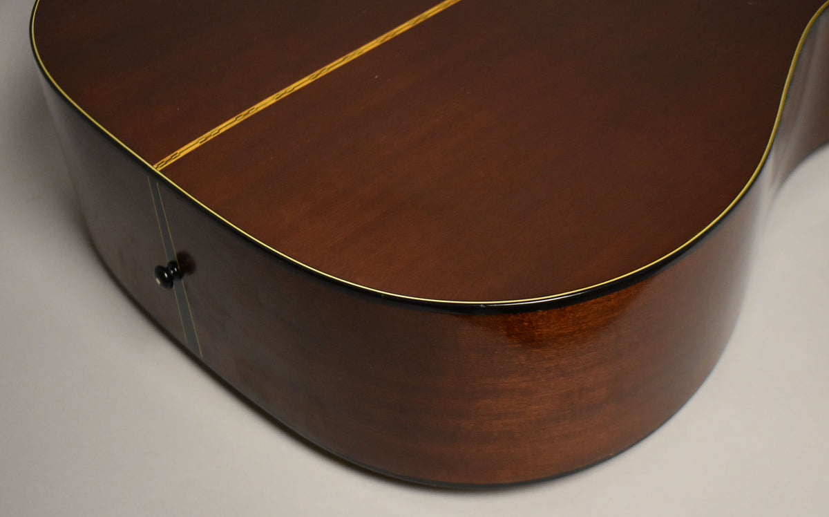 The lower bout of the dark brown acoustic guitar, showing the end pin, binding, and a faint center seam on the back.