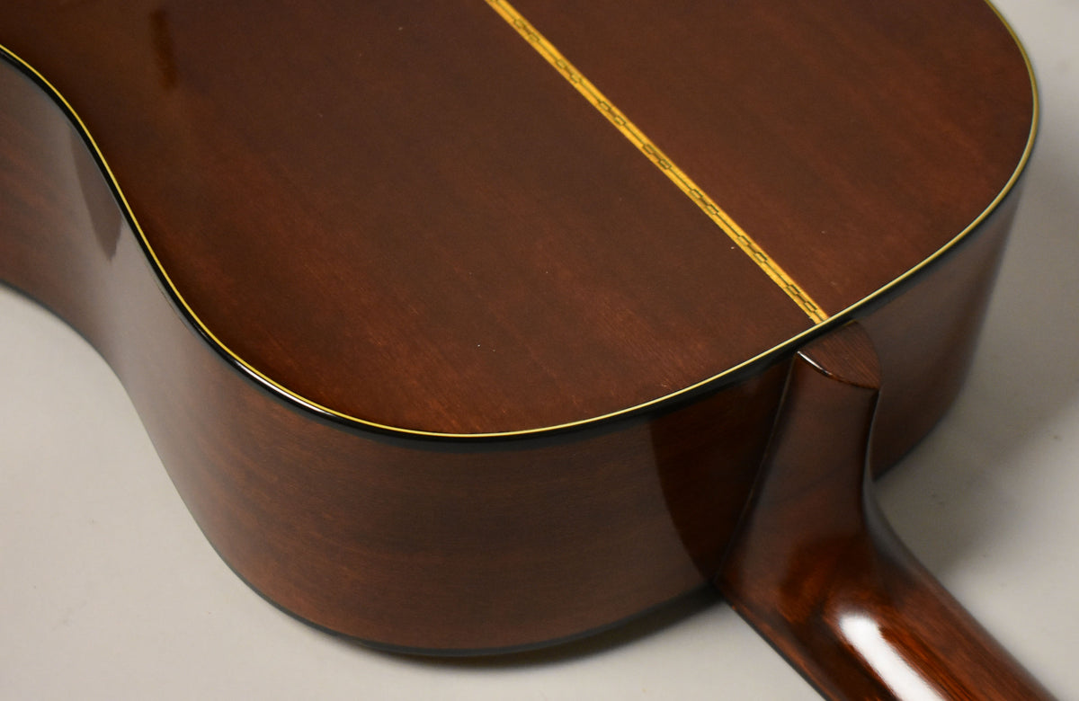 The guitar's dark brown back and side are visible, with a light wood center strip and yellow binding around the edges.
