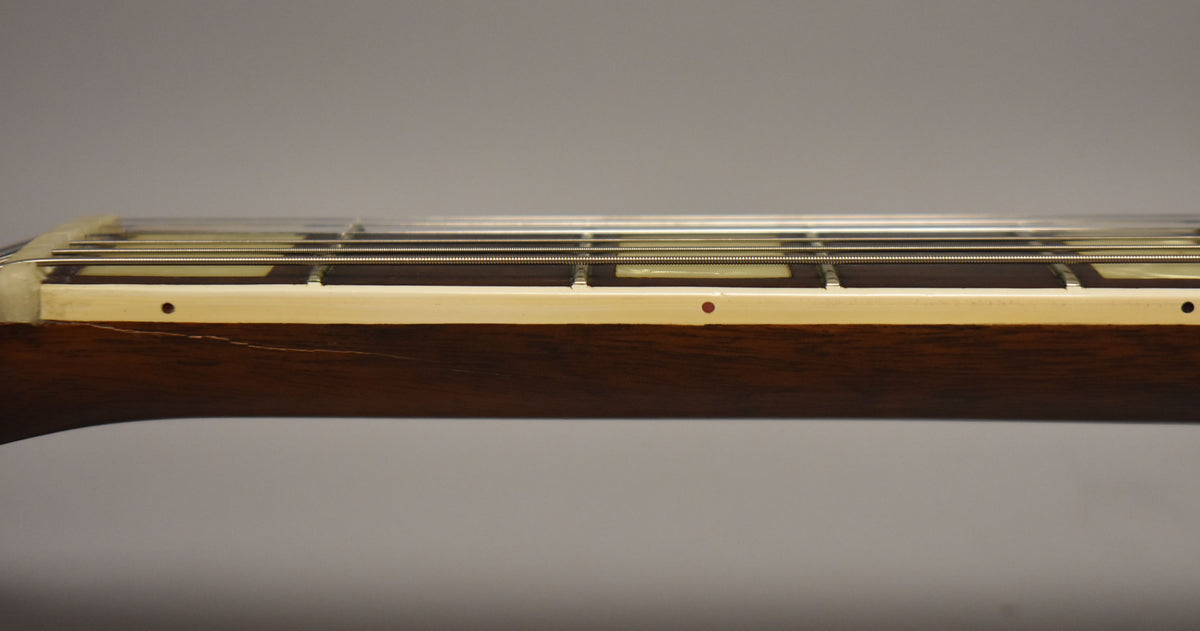 Close-up of the guitar's dark wood neck and cream binding, showing fret markers, strings, and a thin crack in the wood.