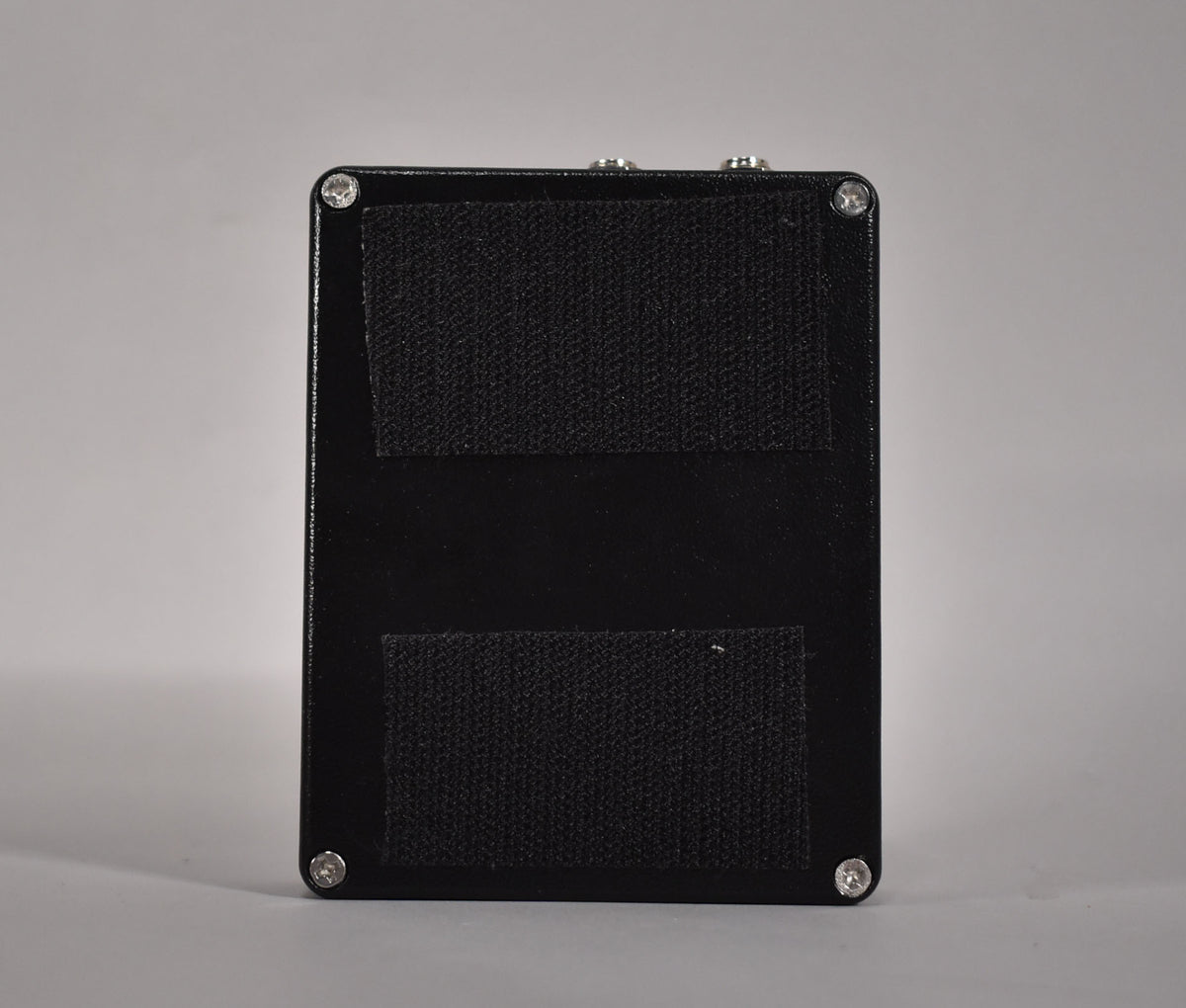The pedal's black bottom plate is visible, with two strips of black hook-and-loop fastener and four silver screws in the corners.