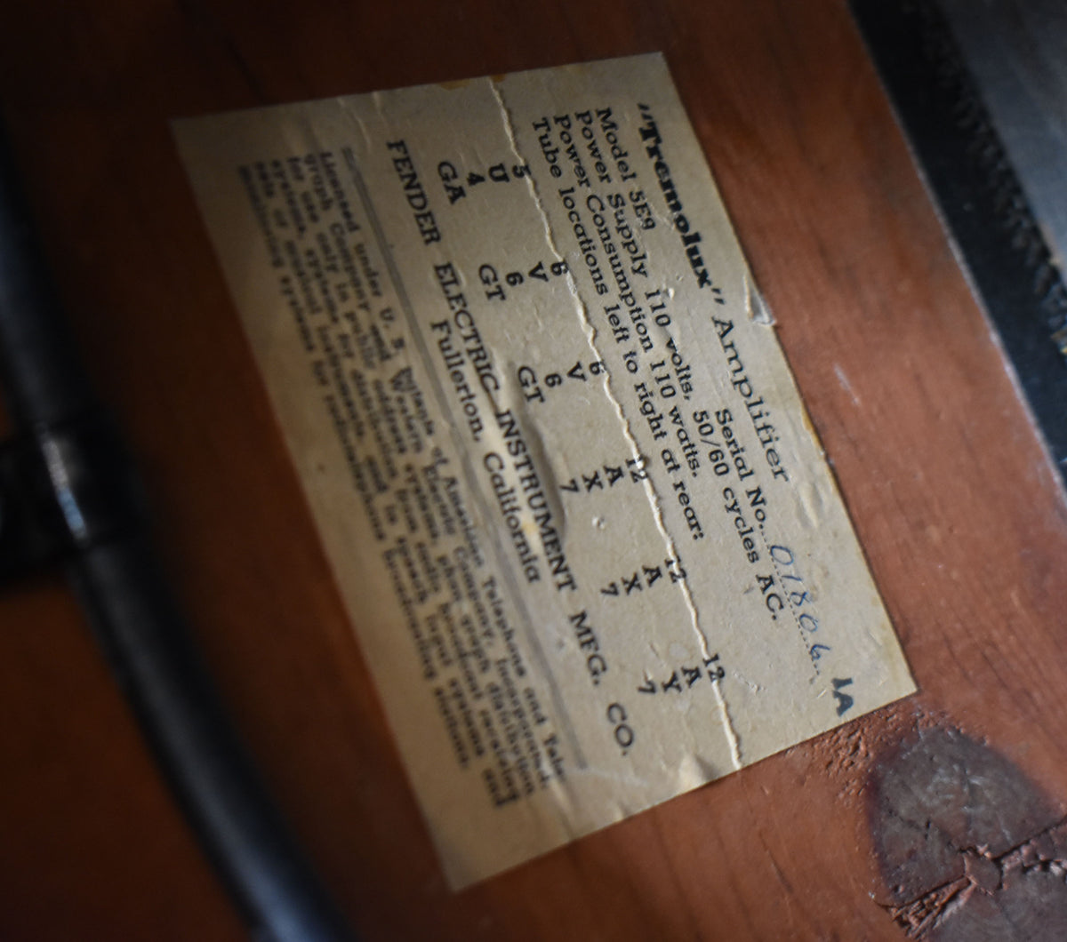 Close-up of the amp's rear panel, showing a worn, creased paper label with specs and a handwritten serial number.
