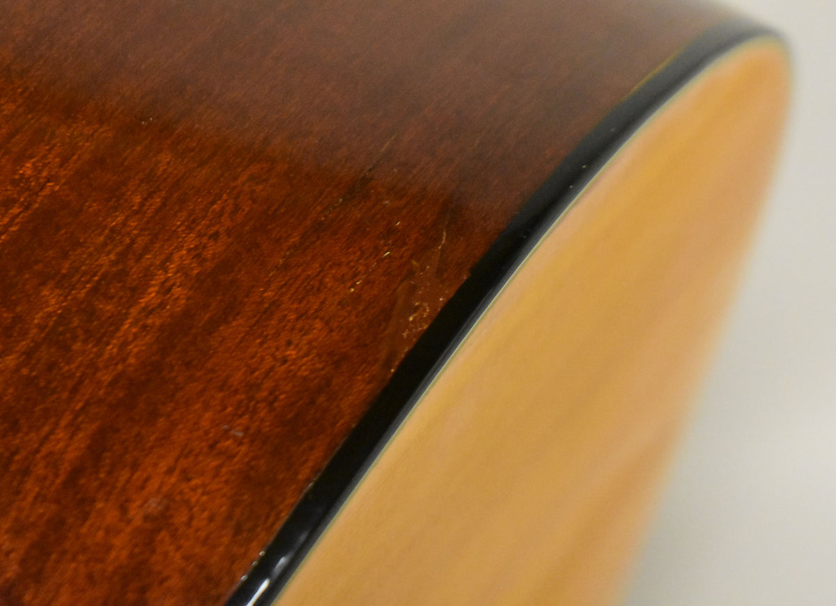 Close-up of the guitar's dark brown back and lighter side, separated by black binding, showing minor surface wear.
