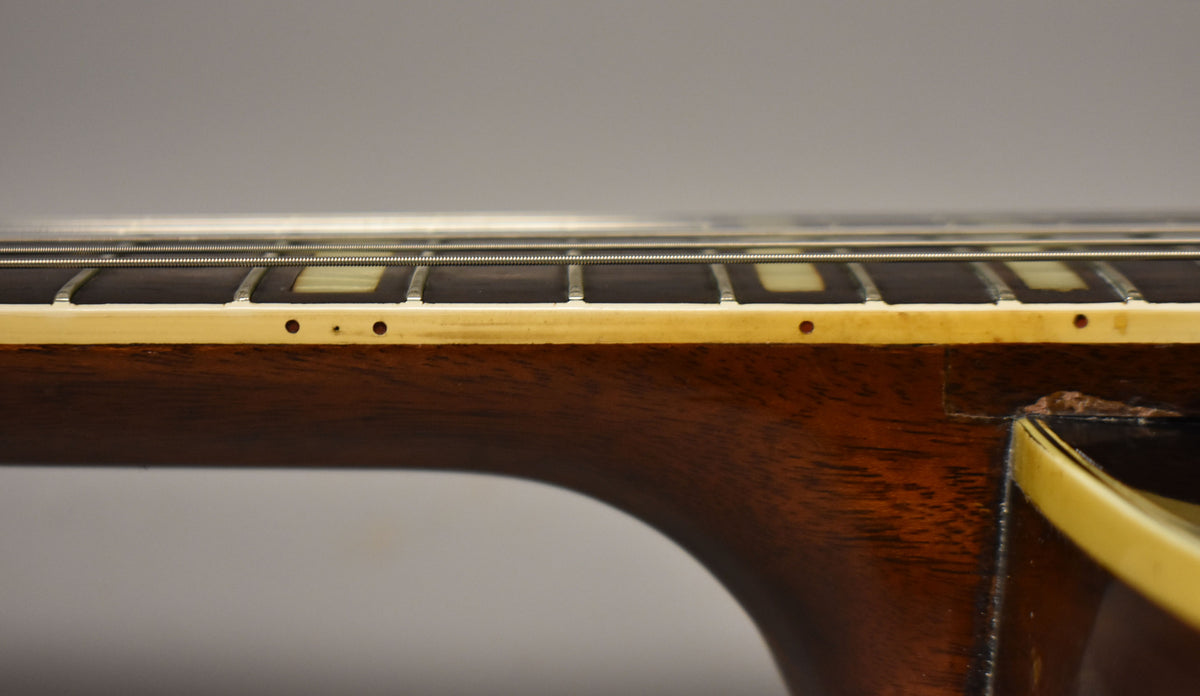 Close-up of the guitar neck, showing the dark fretboard, cream binding with small dots, and a chipped heel joint.