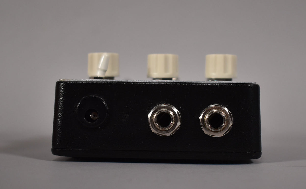 The black textured pedal is viewed from the back, showing a power input and two chrome 1/4-inch jacks.