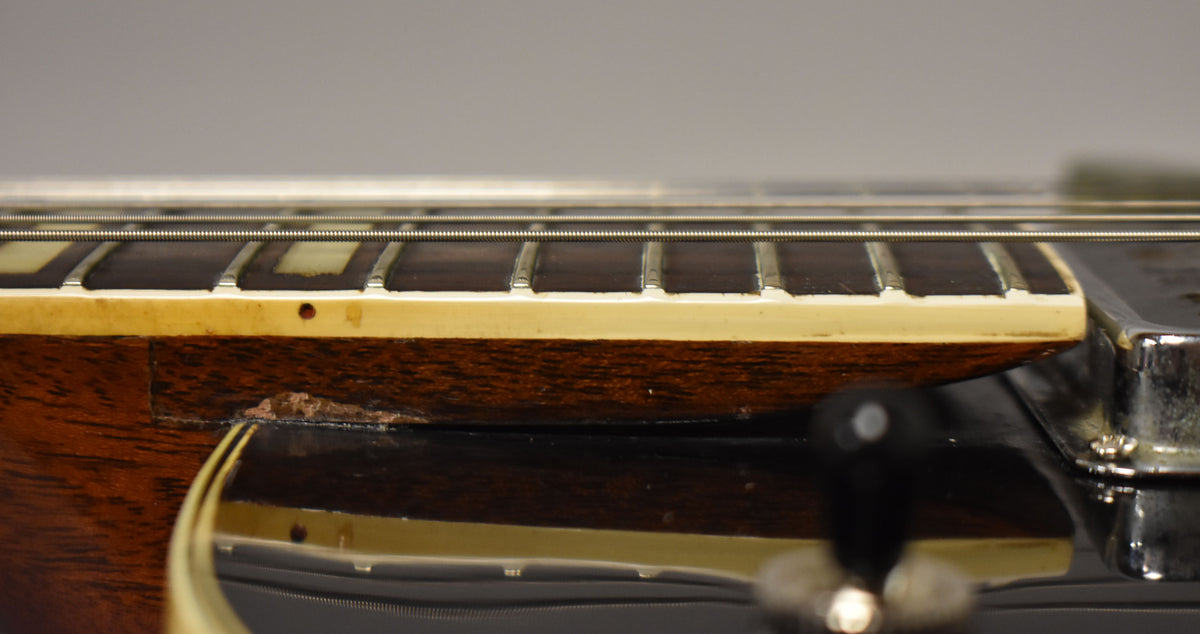 Close-up of the black guitar body and dark brown neck, showing binding separation and finish chipping near the neck joint.