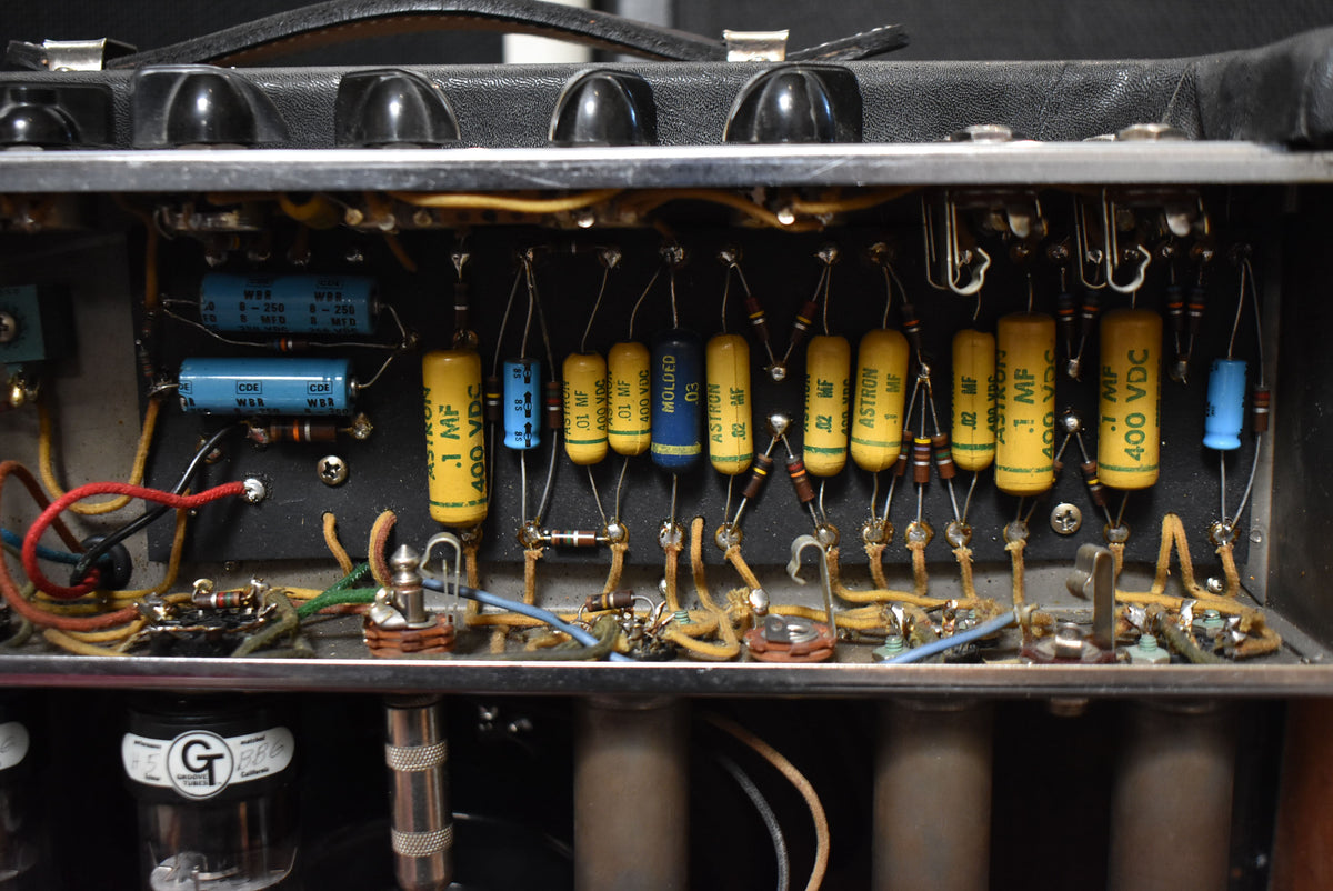 A top-down view of the amp's open chassis, revealing rows of yellow and blue capacitors, resistors, and wiring.