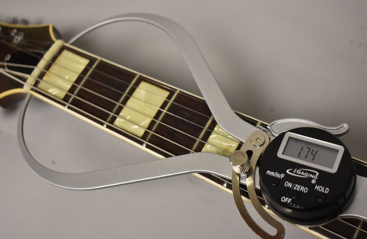 Close-up of the guitar's dark fretboard with rectangular pearloid inlays, showing a digital caliper measuring the fret height at 1.74.