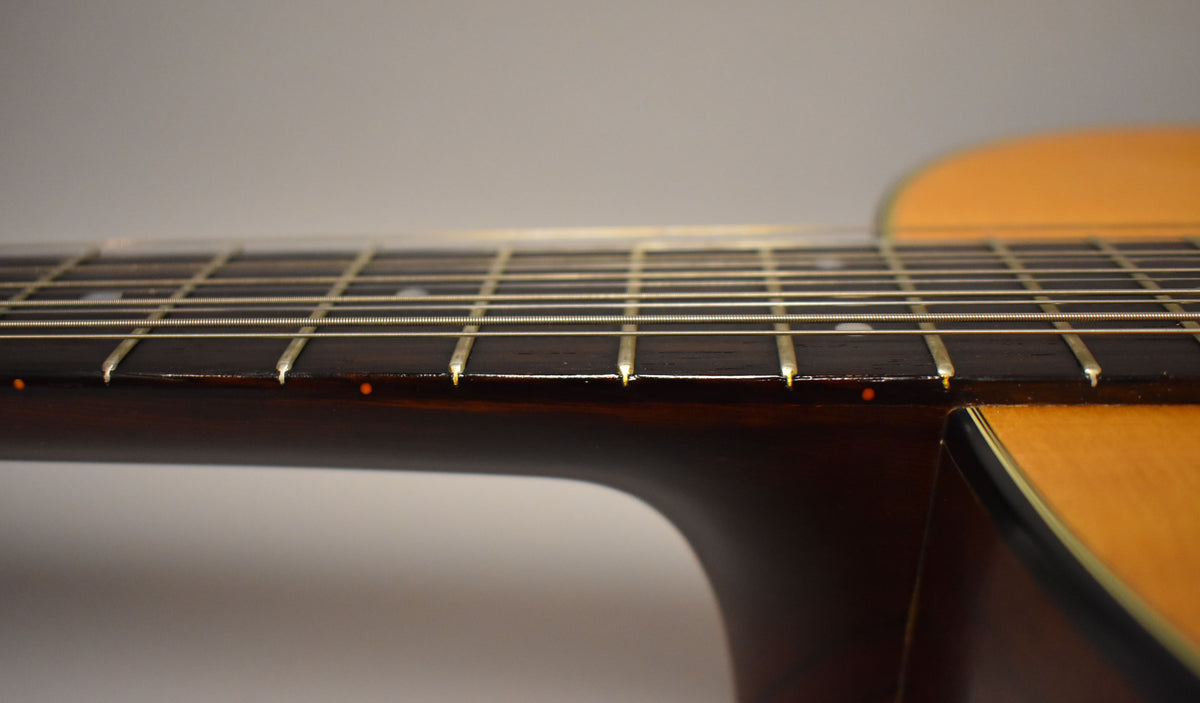 Close-up of the dark fretboard and neck, showing light fret wear and orange side dots, with the natural body visible on the right.