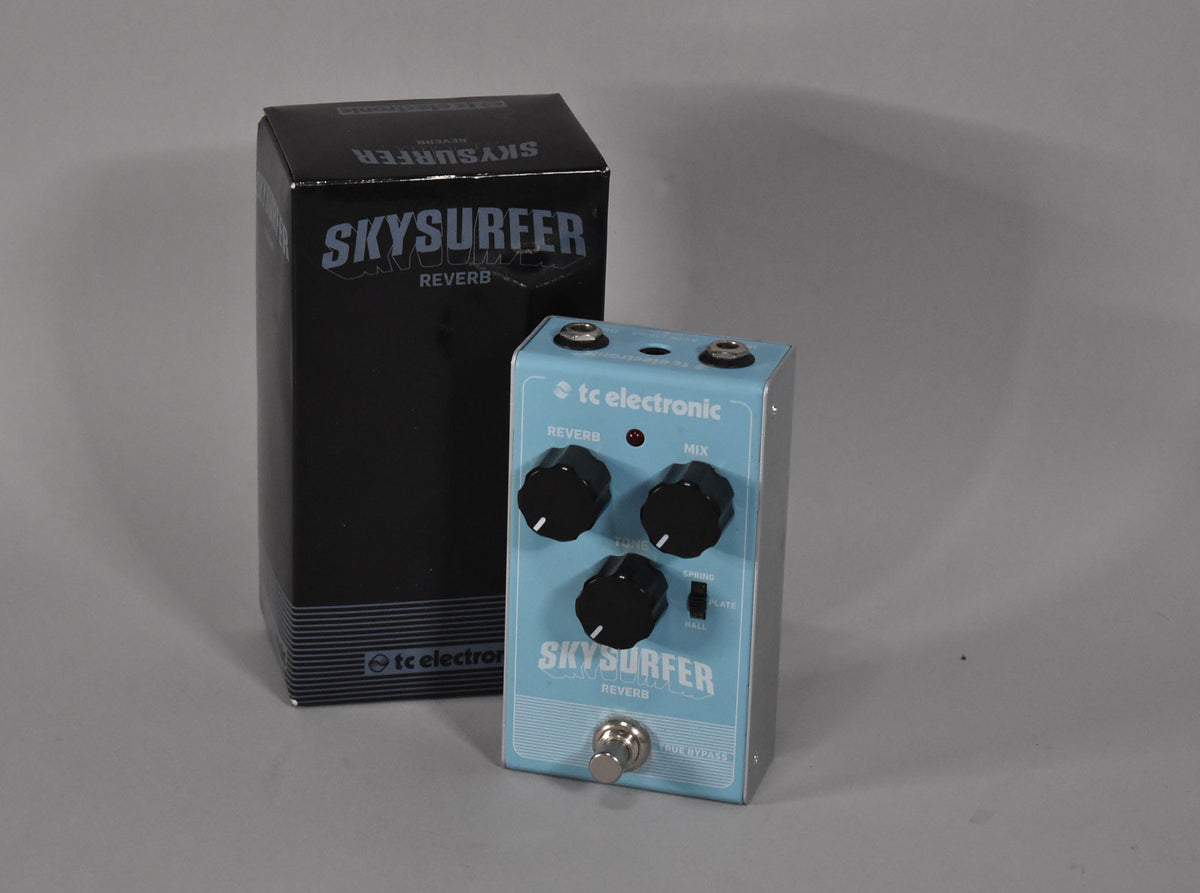 A light blue reverb pedal with three black knobs and a toggle switch, next to its black box.