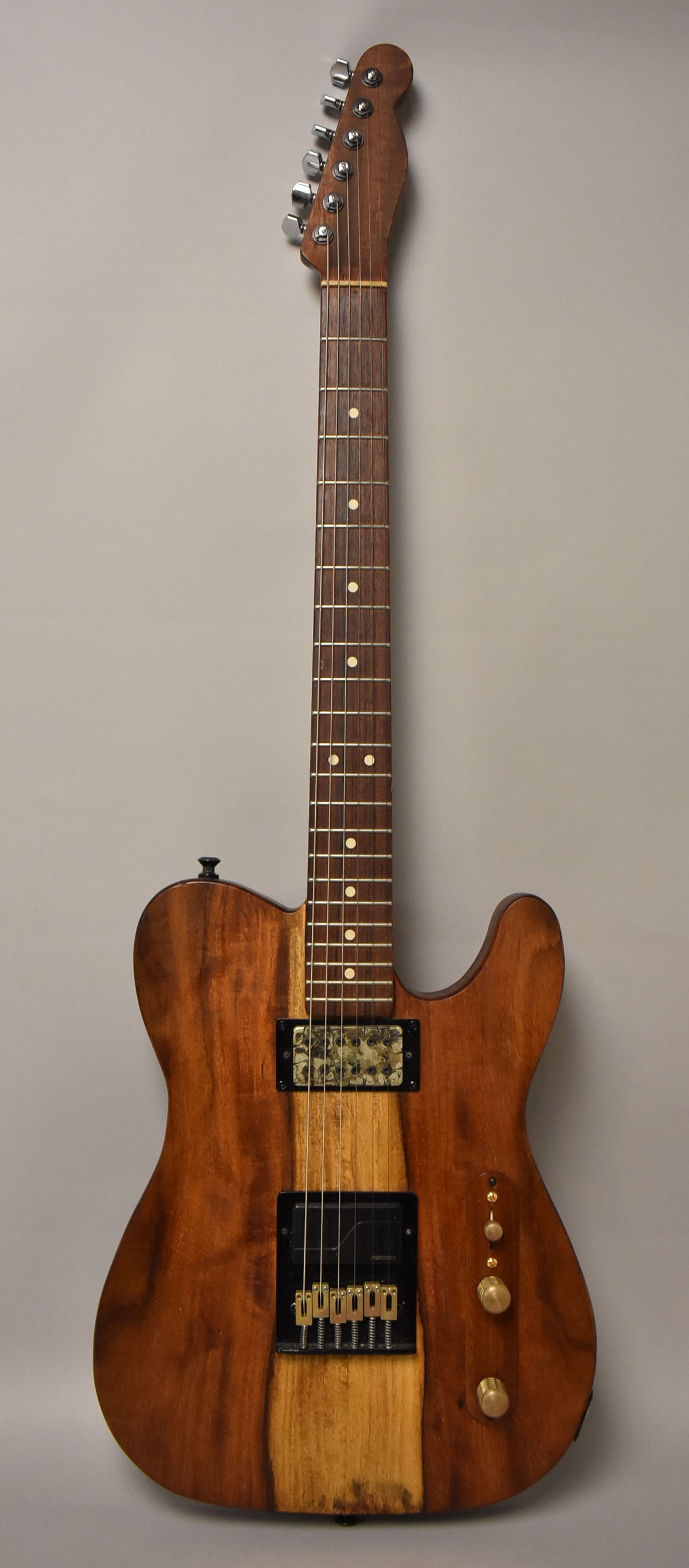 Full-length view of a natural finish T-style guitar with a dark wood body, light wood stripe, two humbuckers, and gold hardware.