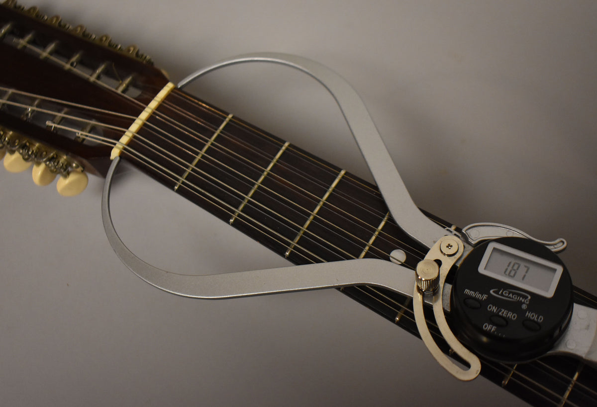 A close-up of the dark fretboard and nut, with a silver digital caliper measuring the nut width at 1.87 inches.