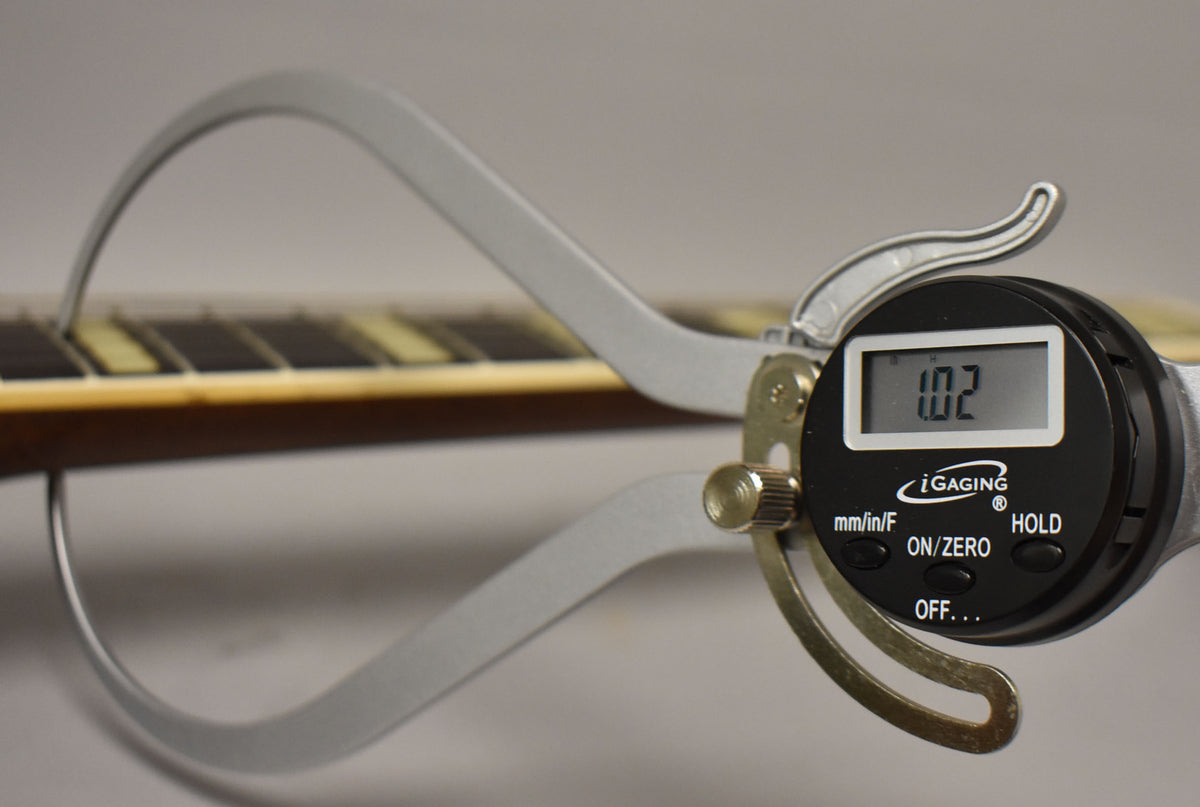 A digital caliper measures the fret height on the guitar's dark brown neck, showing 1.02 on its display.
