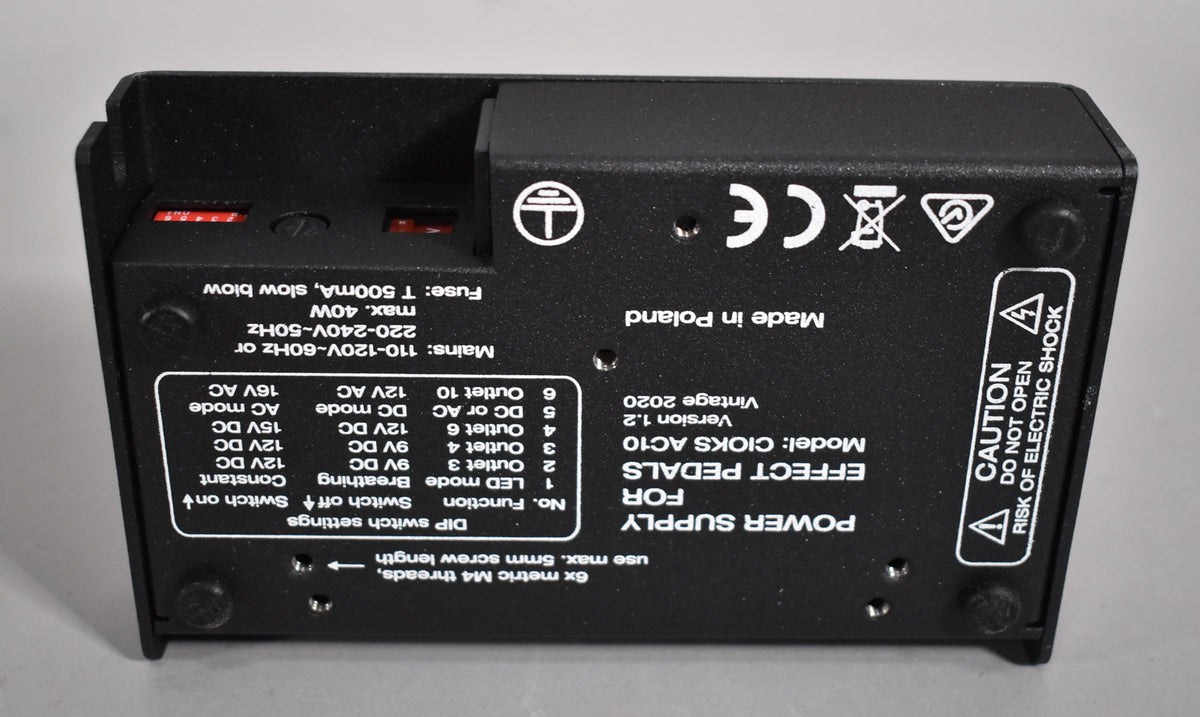 The black power supply is seen from above, showing its underside with four rubber feet and two red DIP switches.
