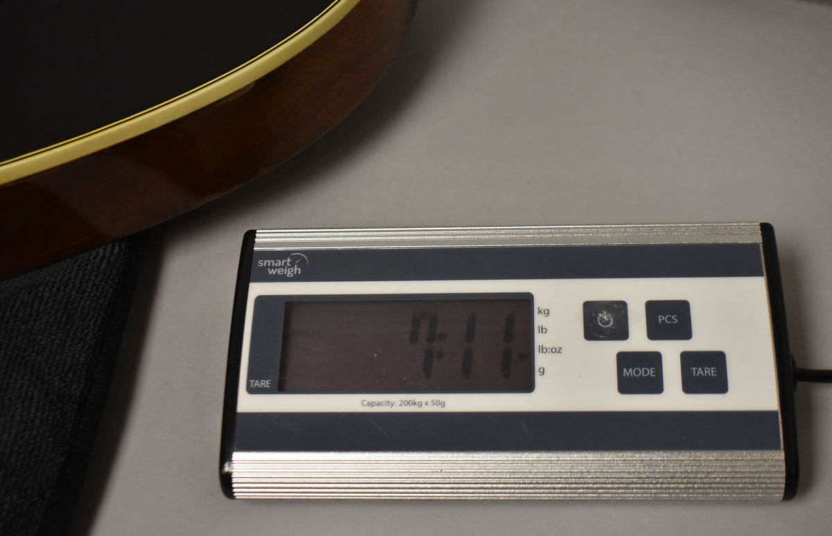 The guitar's dark brown body edge with cream binding is visible above a digital scale displaying "7.11" lbs.