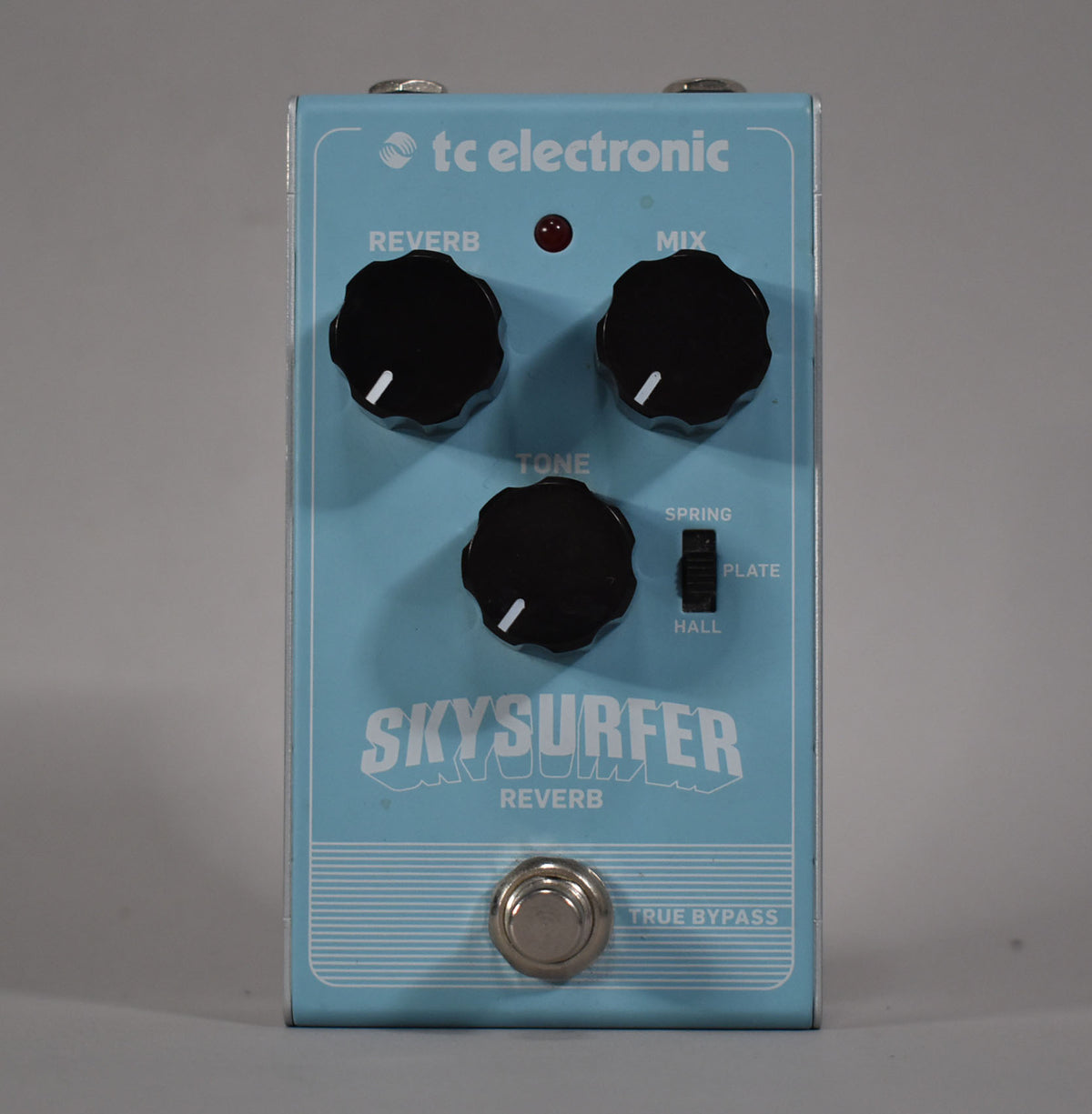 Light blue reverb pedal, viewed from the front, with three black control knobs, a red LED, a three-way toggle switch, and a footswitch.