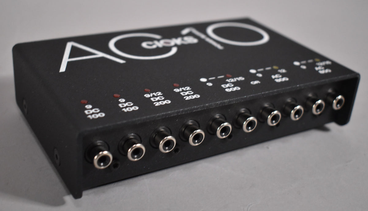 A black power supply with a matte finish, viewed from the front-right, showing ten silver-ringed power outputs and red indicator lights.
