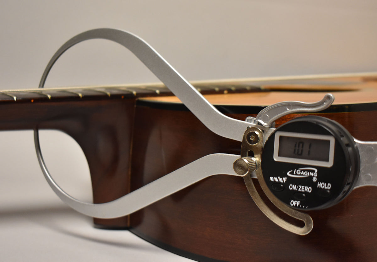 A digital caliper measures the neck relief at the 7th fret, showing 1.01mm, against the dark brown back and natural top.